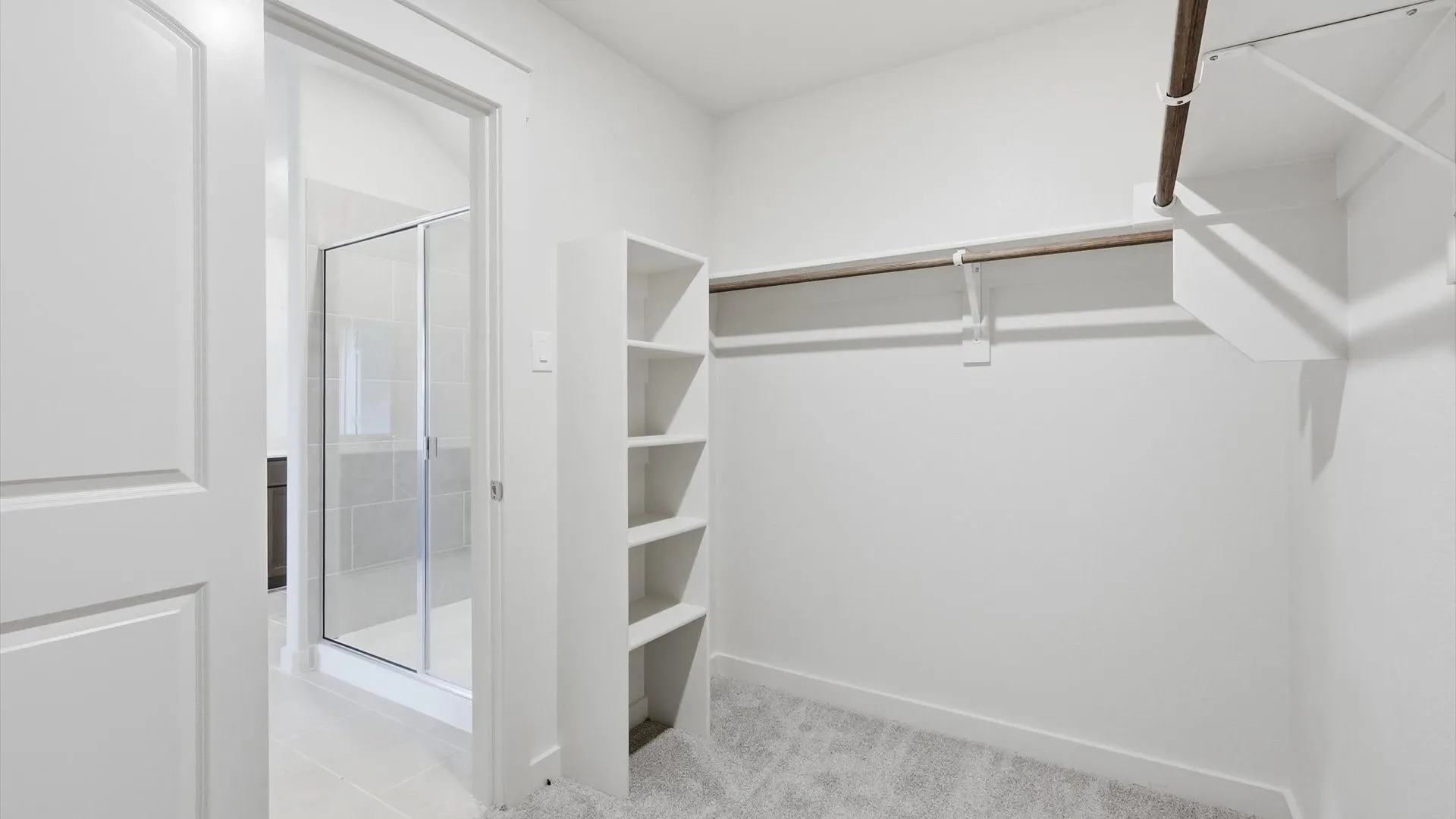 Walk-in closet featuring built-in shelving, carpet flooring, and clothing rods, with direct access to a bathroom with a glass-enclosed shower