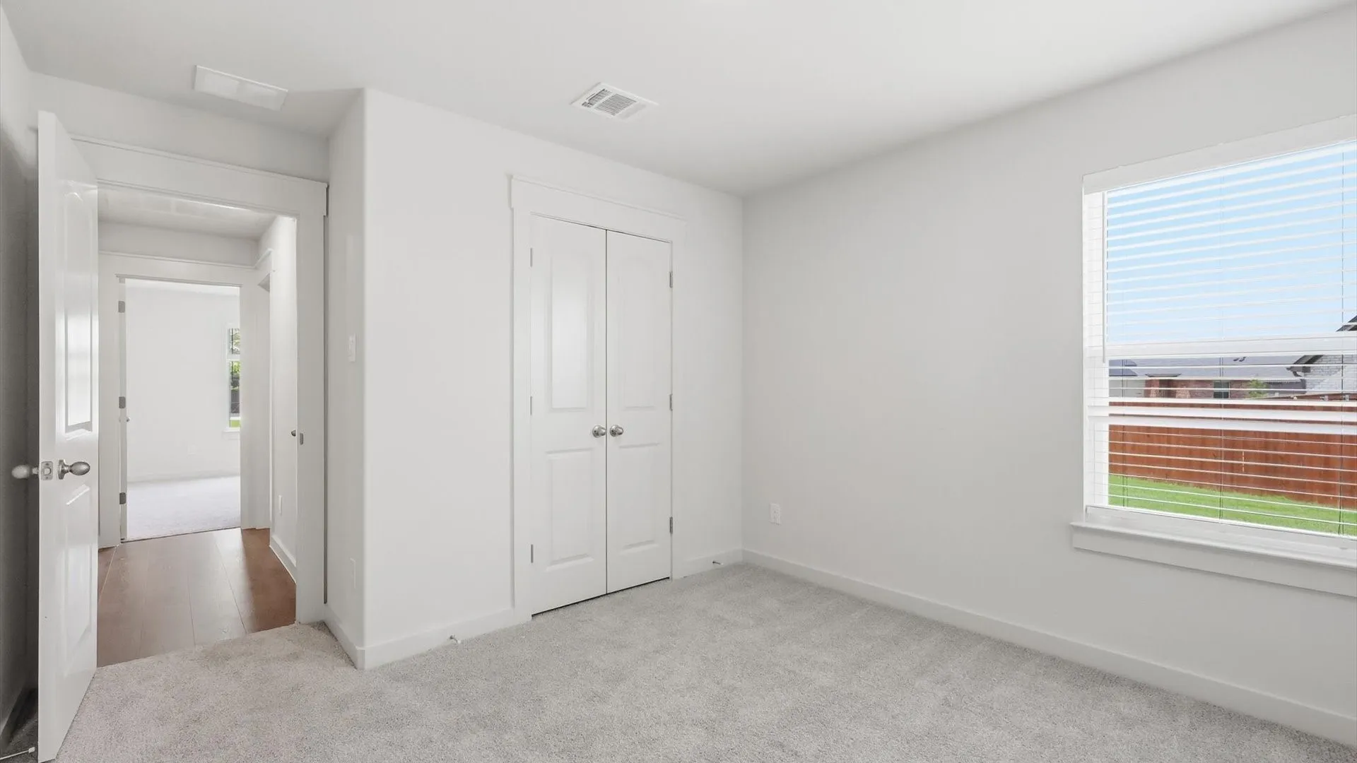 Carpeted room with a double-door closet, a window with blinds, and white trim throughout