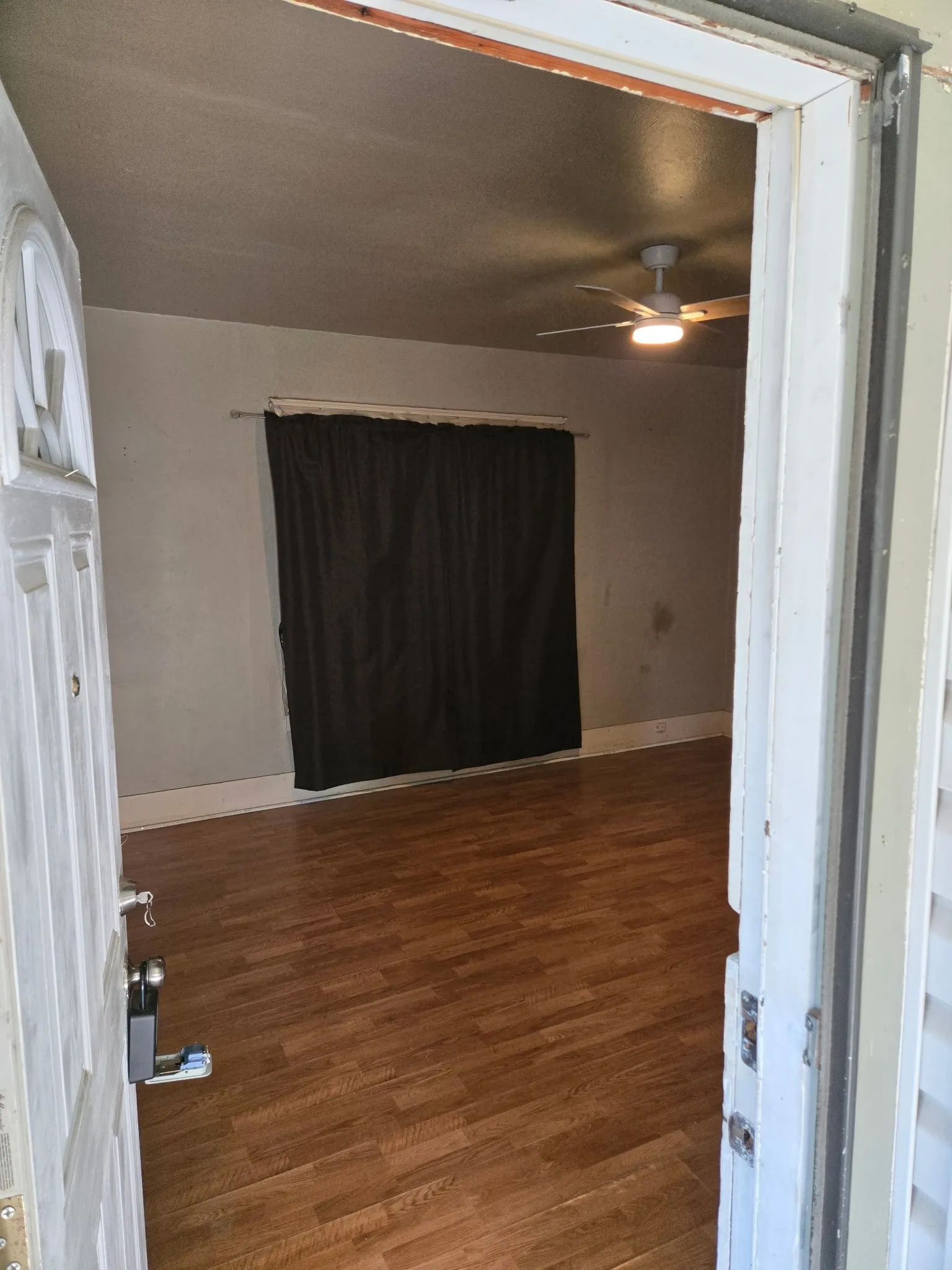 Interior space featuring wood-finish flooring, a ceiling fan with integrated lighting, and window with dark curtain