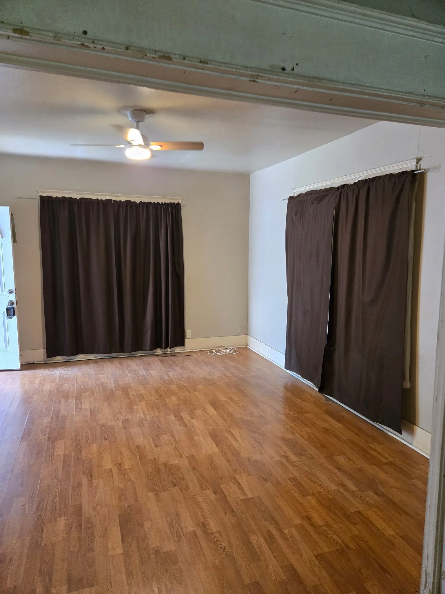 Spacious interior room featuring wood-finish flooring, two window openings, and a ceiling fan with integrated lighting