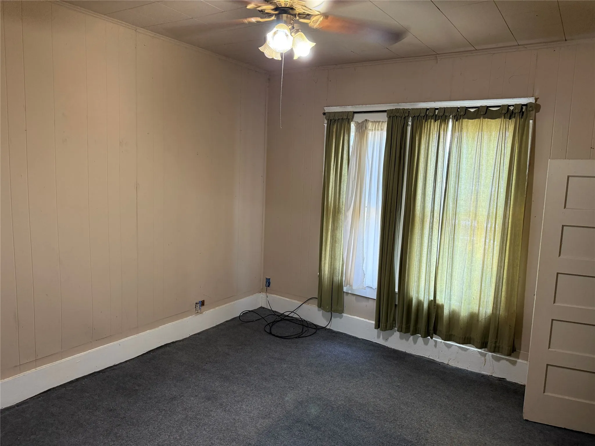 Room featuring panel walls, wall-to-wall carpeting, and a ceiling fan