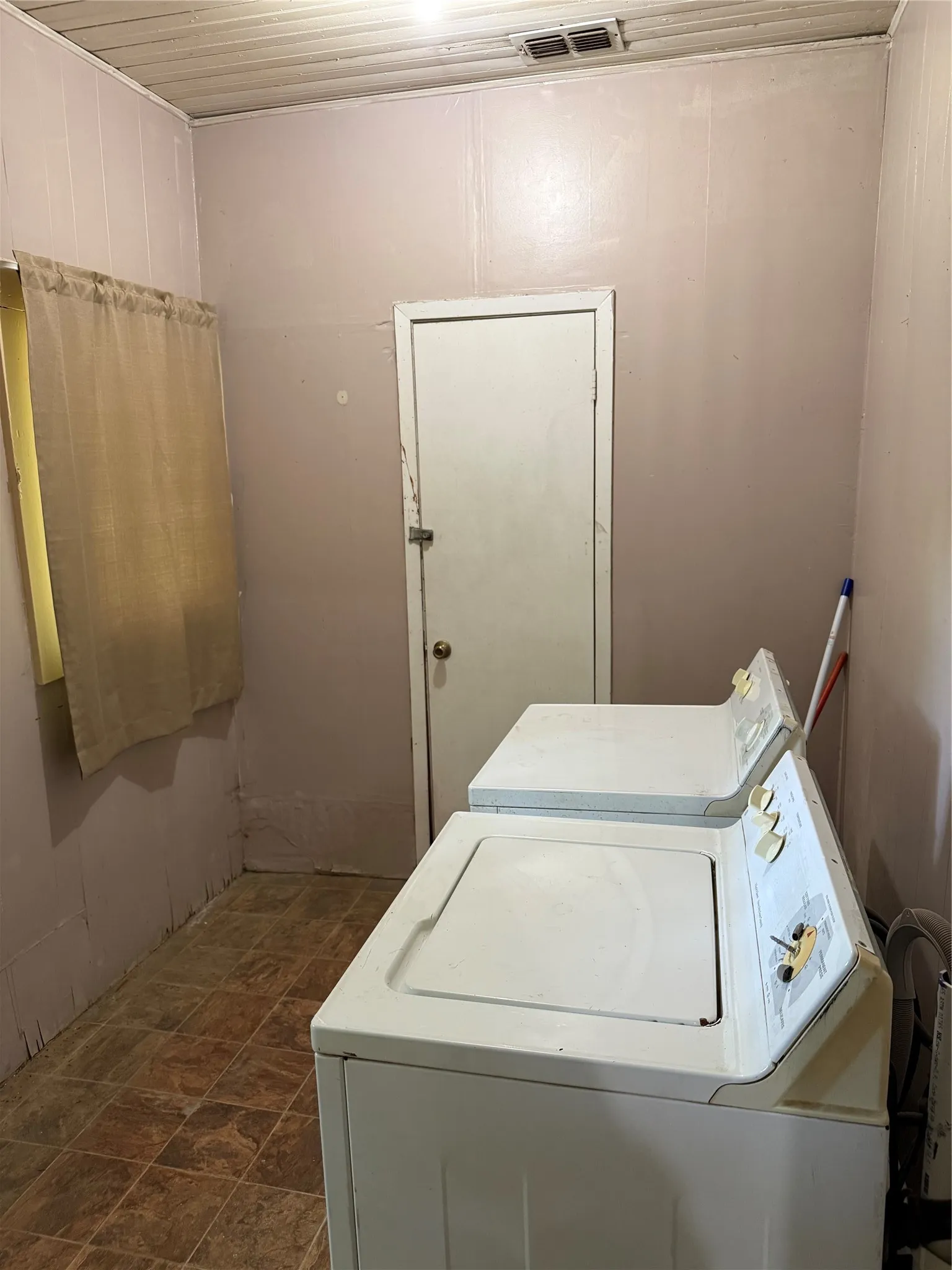 Utility area featuring tile-look flooring, light-toned wall paneling, and a white ceiling with ventilation