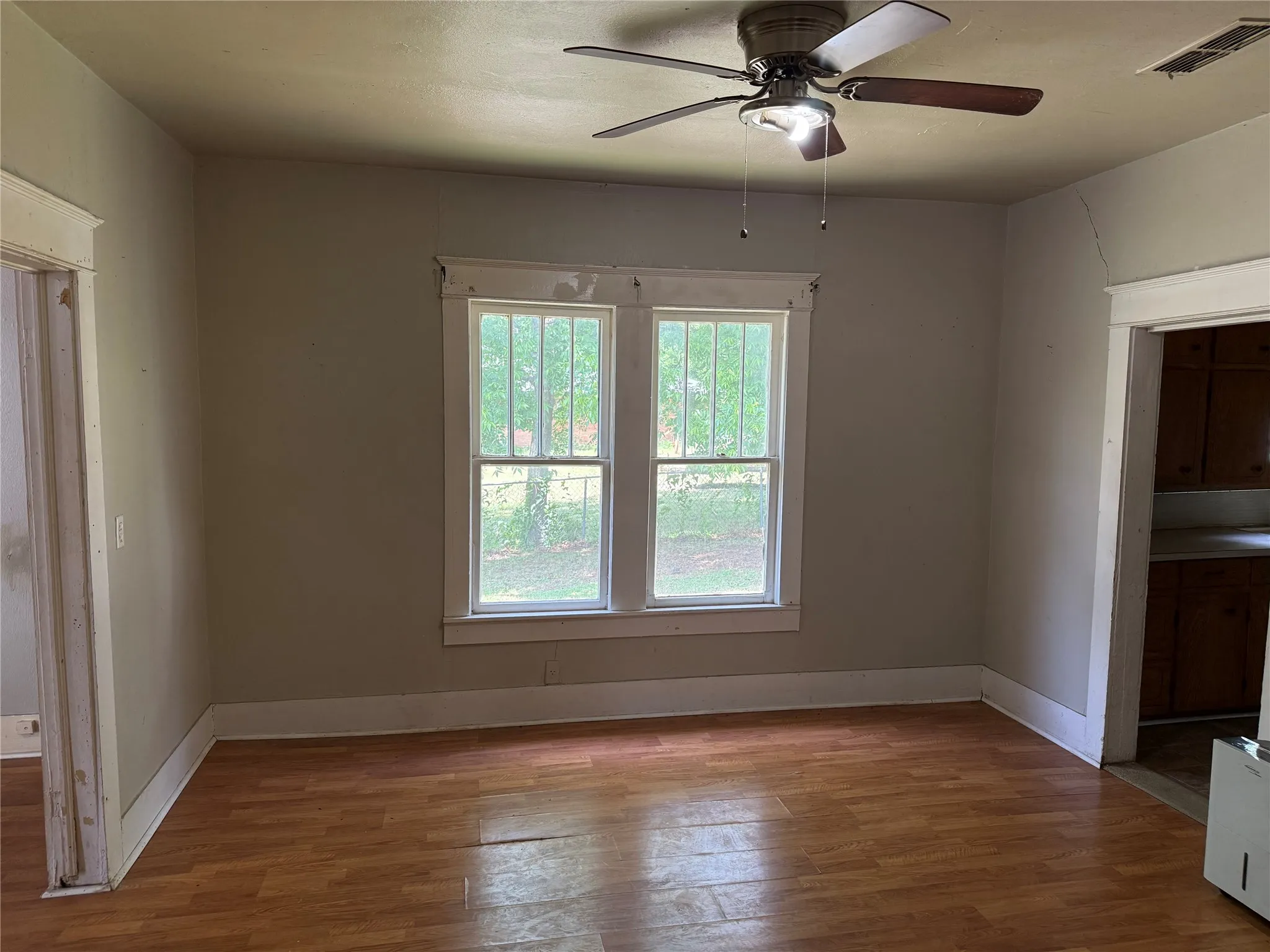 Interior room featuring wood-finish flooring, two large windows, painted walls, and a ceiling fan with integrated lighting