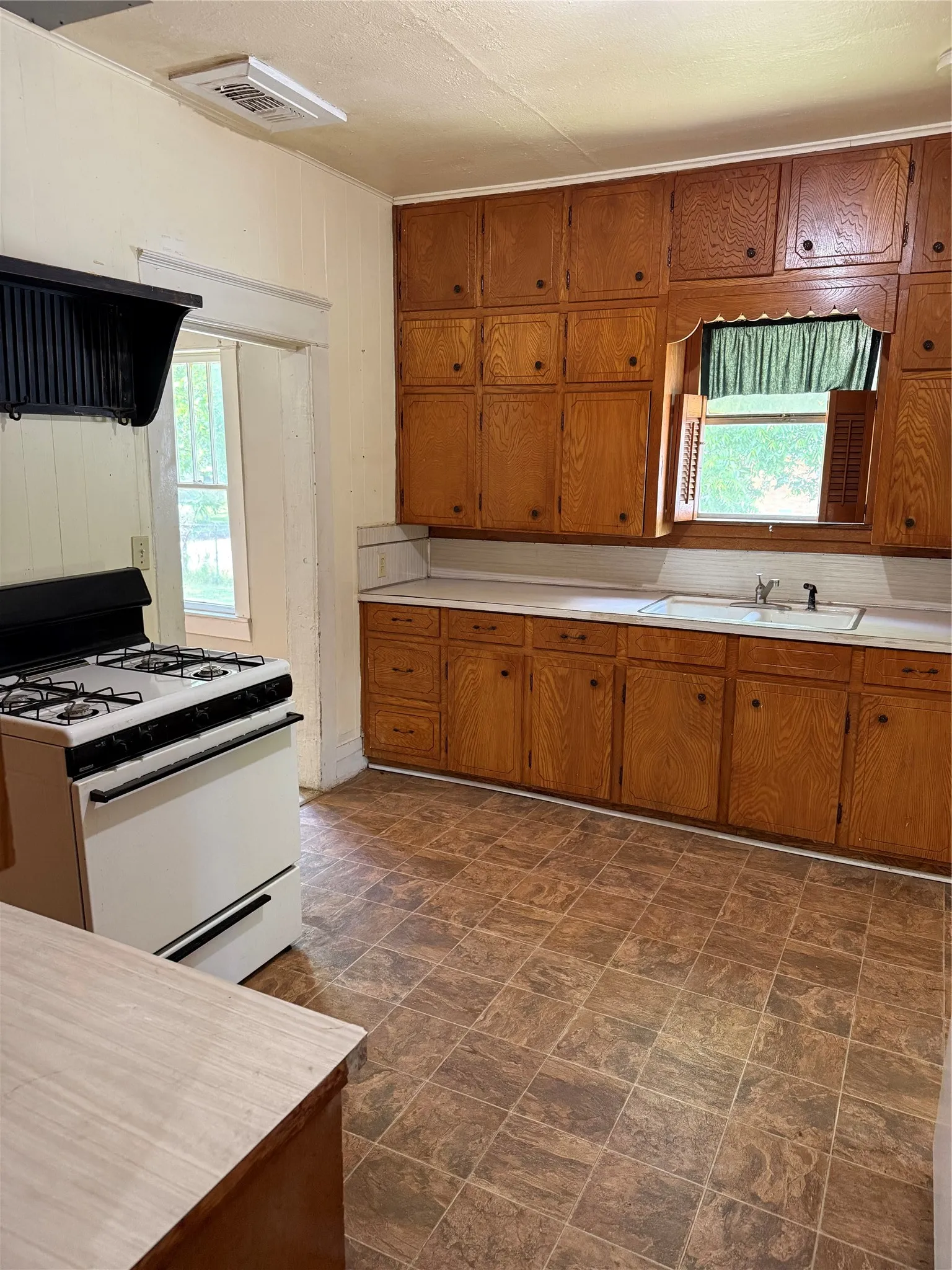 Kitchen featuring extensive wood cabinetry, a built-in window with wooden shutters, white countertops, a gas range, and patterned floor​​‌​​​​‌​​‌‌​‌‌​​​‌‌​‌​‌​‌​​​‌​​ tiles