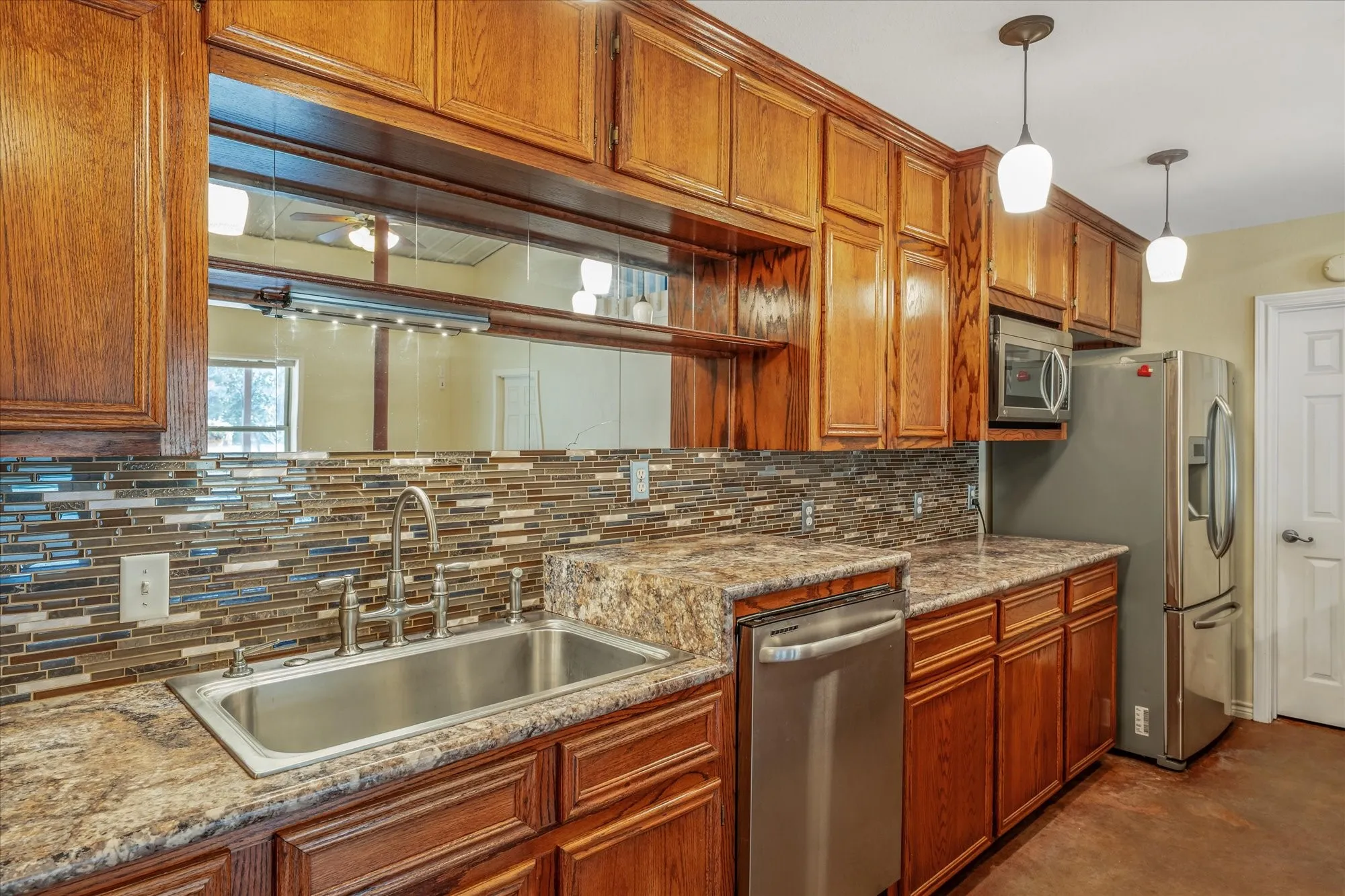 Kitchen with wood finish cabinetry, stainless steel appliances, hanging light fixtures, and light stone counters