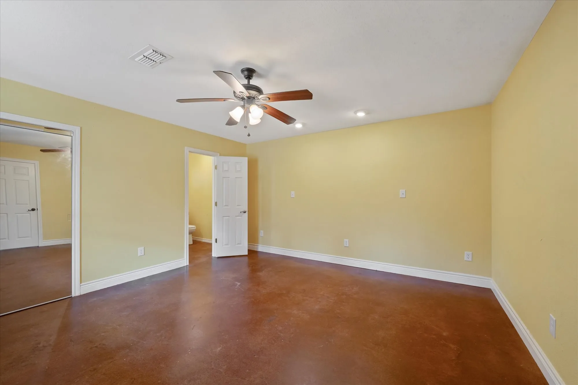 Unfurnished bedroom featuring finished concrete flooring, a ceiling fan, and ensuite bath