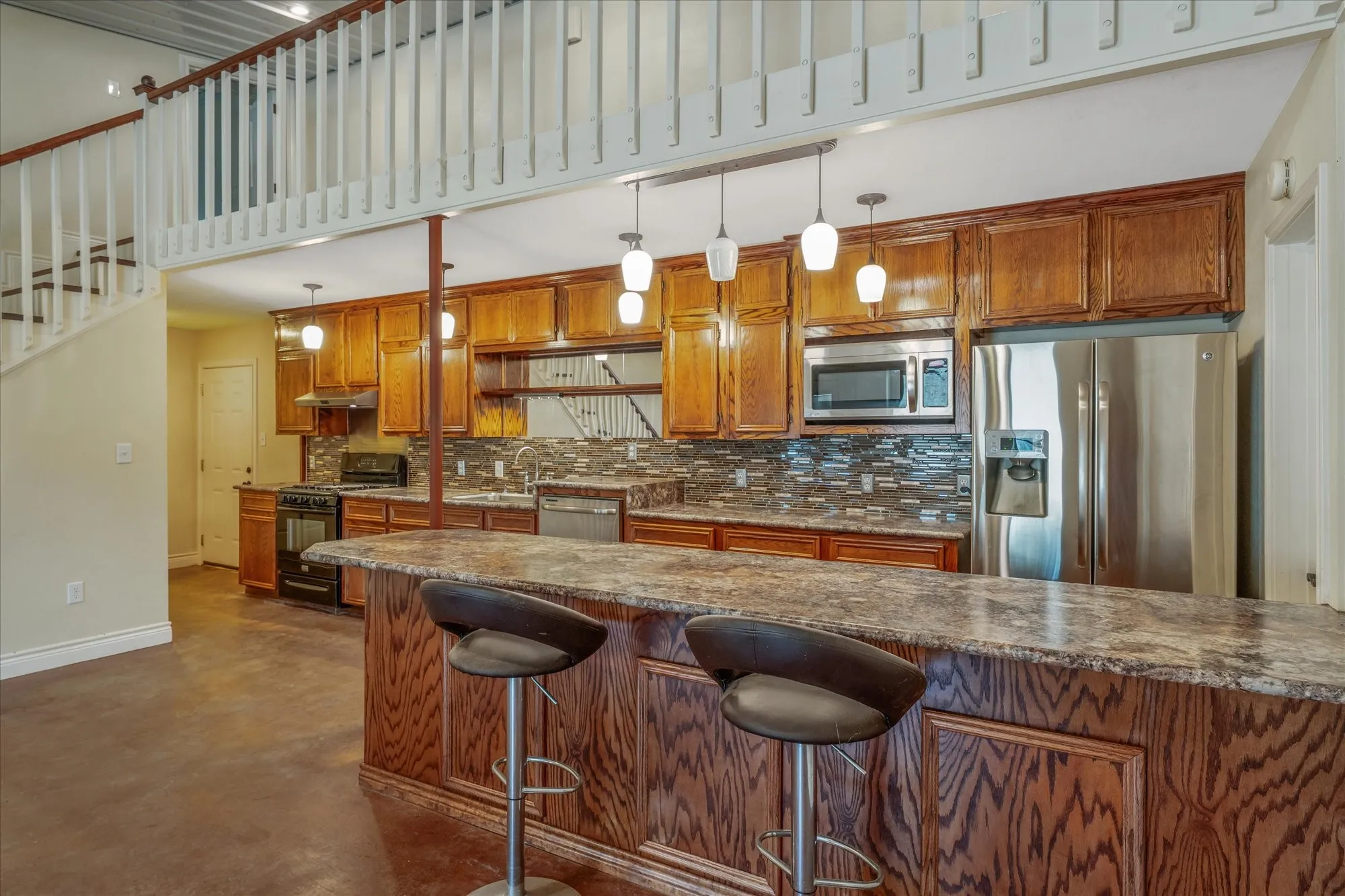 Kitchen featuring wood finish cabinets, stainless steel appliances, a breakfast bar area, finished concrete flooring, and dark stone counters