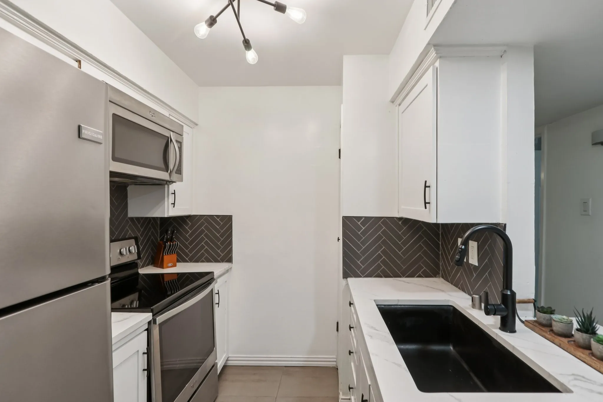 Kitchen featuring stainless steel appliances, white cabinetry, light tile patterned floors, and light stone counters