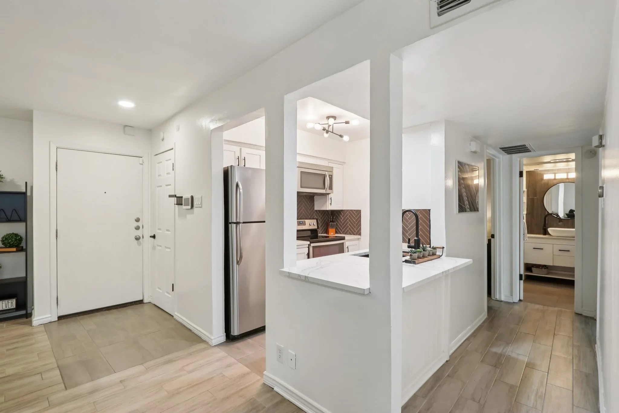 Kitchen featuring wood tiled floors, stainless steel appliances, a peninsula, white cabinets, and backsplash