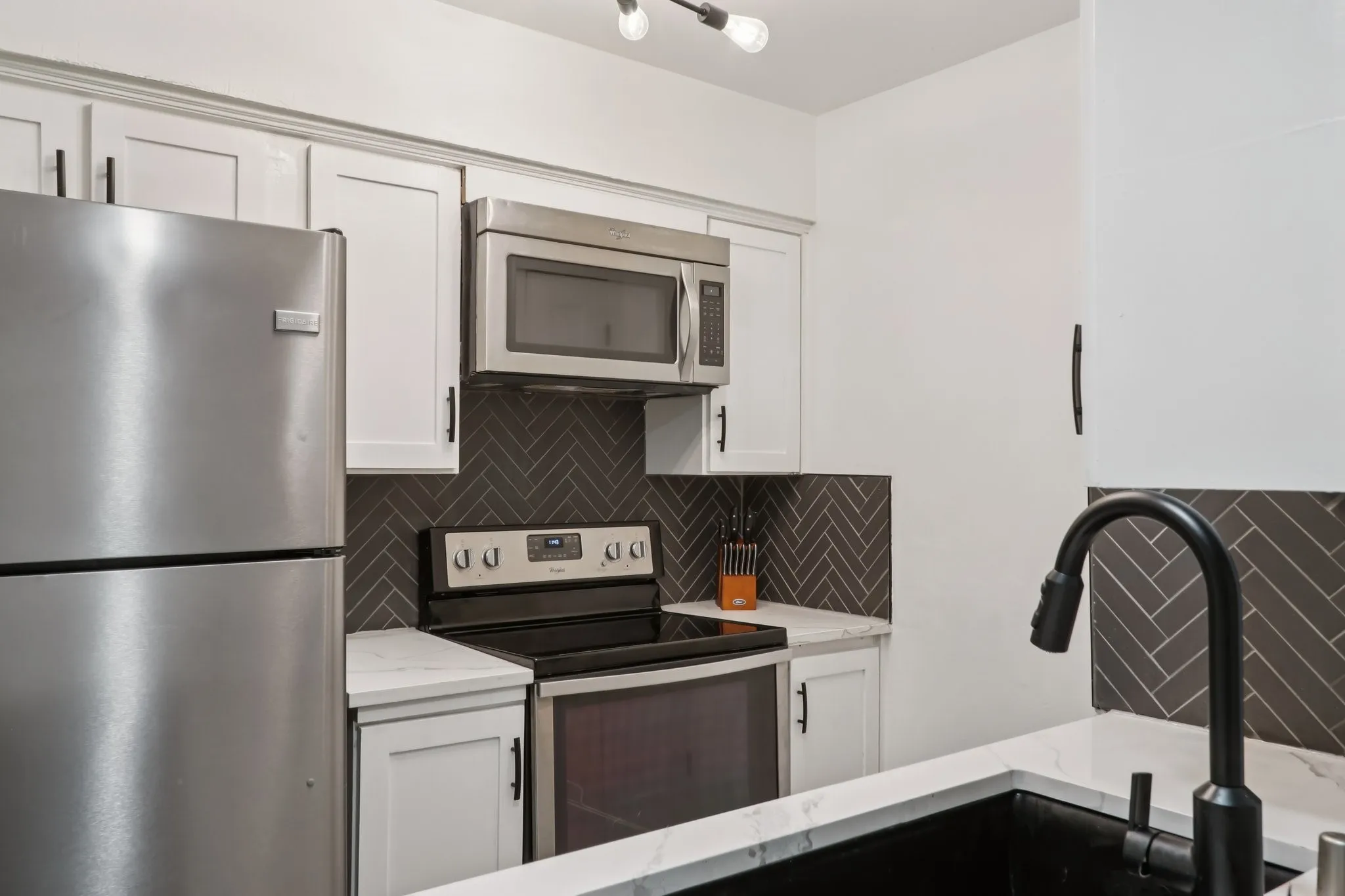 Kitchen with stainless steel appliances, decorative backsplash, white cabinets, and light stone countertops