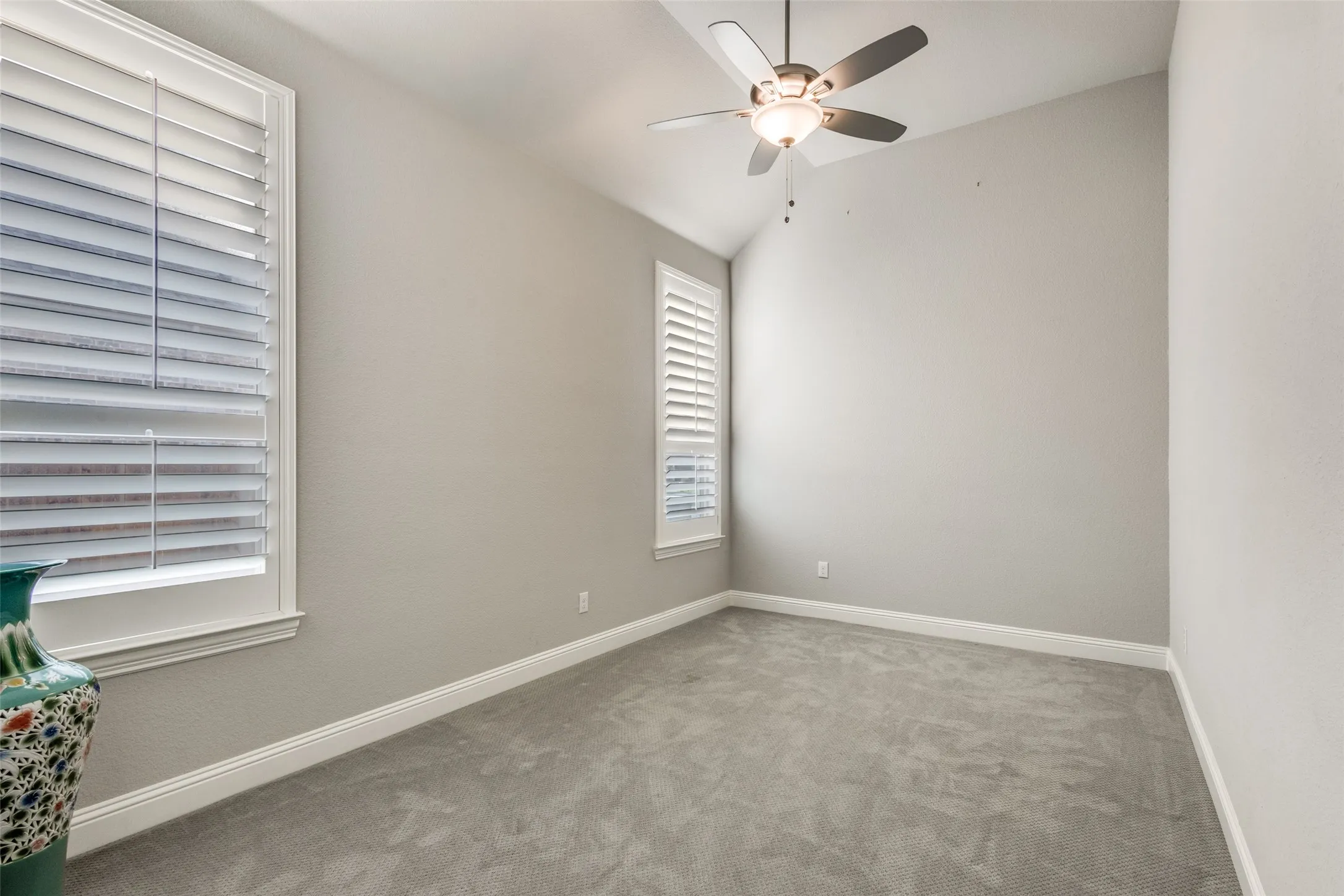 Spare room featuring ceiling fan, light carpet, and vaulted ceiling