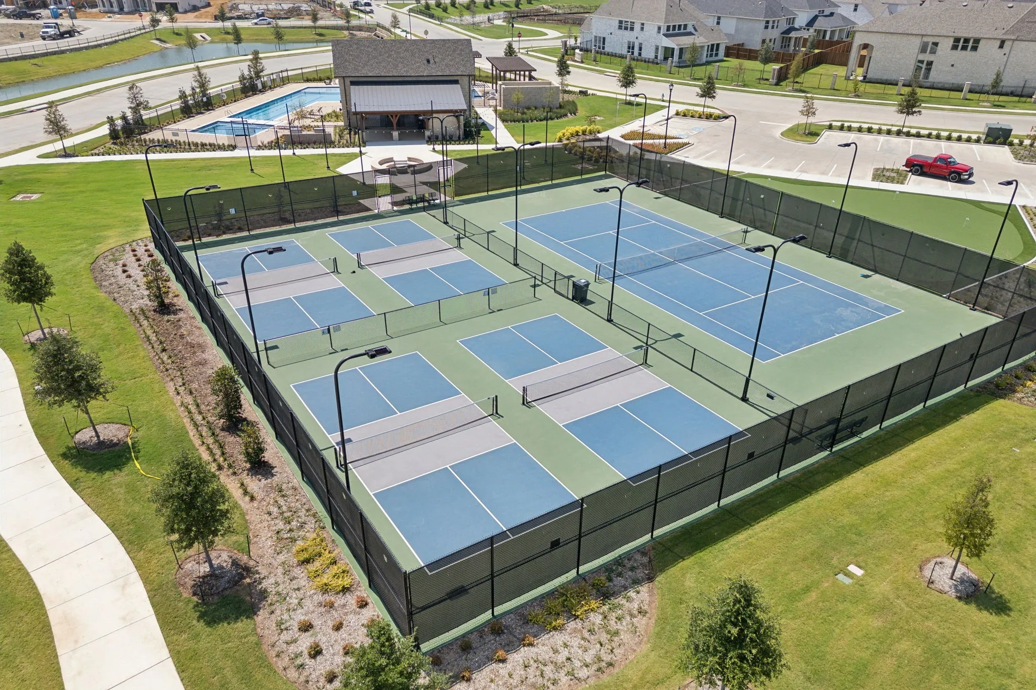 Fenced athletic courts featuring multiple pickleball courts and a full-size tennis court with integrated lighting