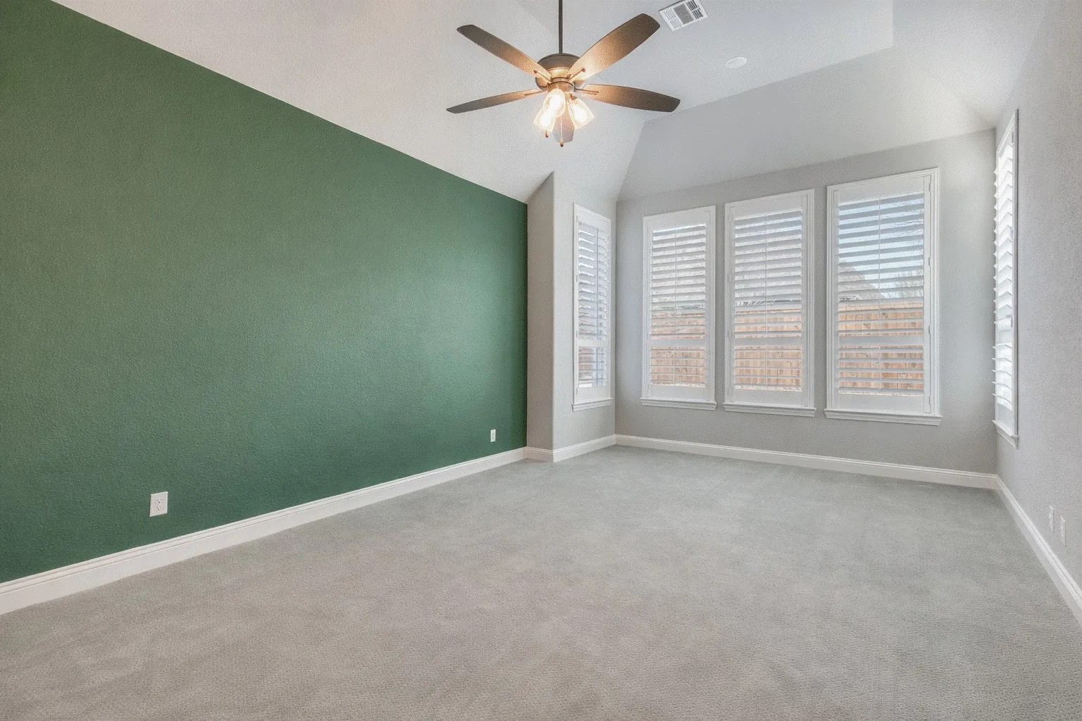 Primary bedroom with a ceiling fan, light colored carpet, and vaulted ceiling