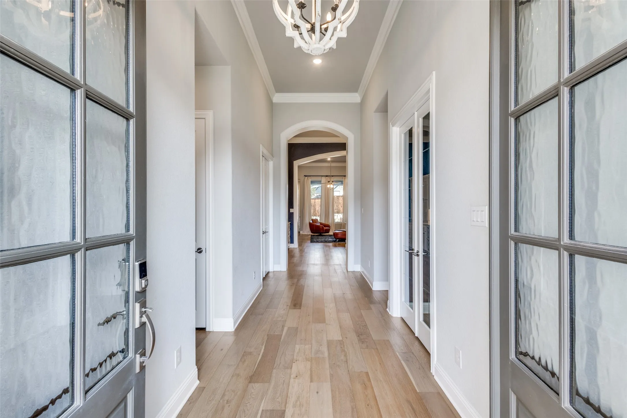Entrance foyer featuring arched walkways, ornamental molding, light wood-style flooring, suspended lighting, and french doors