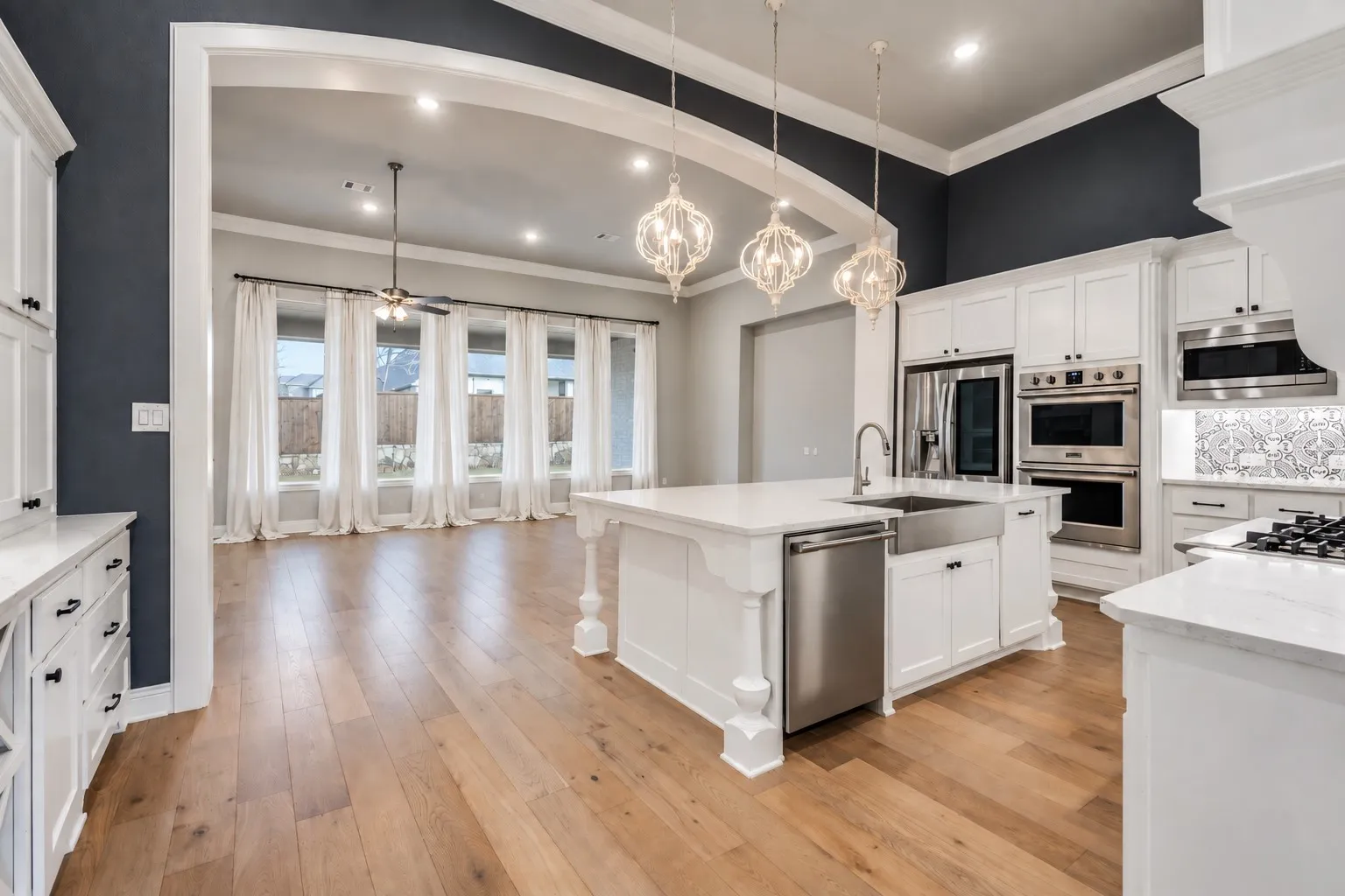 Open-concept kitchen with a large central island, farmhouse sink, stainless steel appliances, and white cabinetry