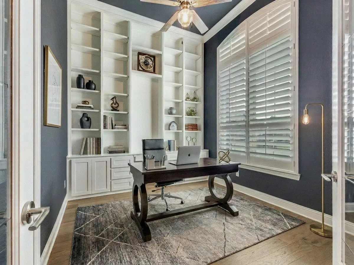 Home office featuring crown molding, wood shutters, light hardwood flooring, and built-in shelving.  AI staged photo