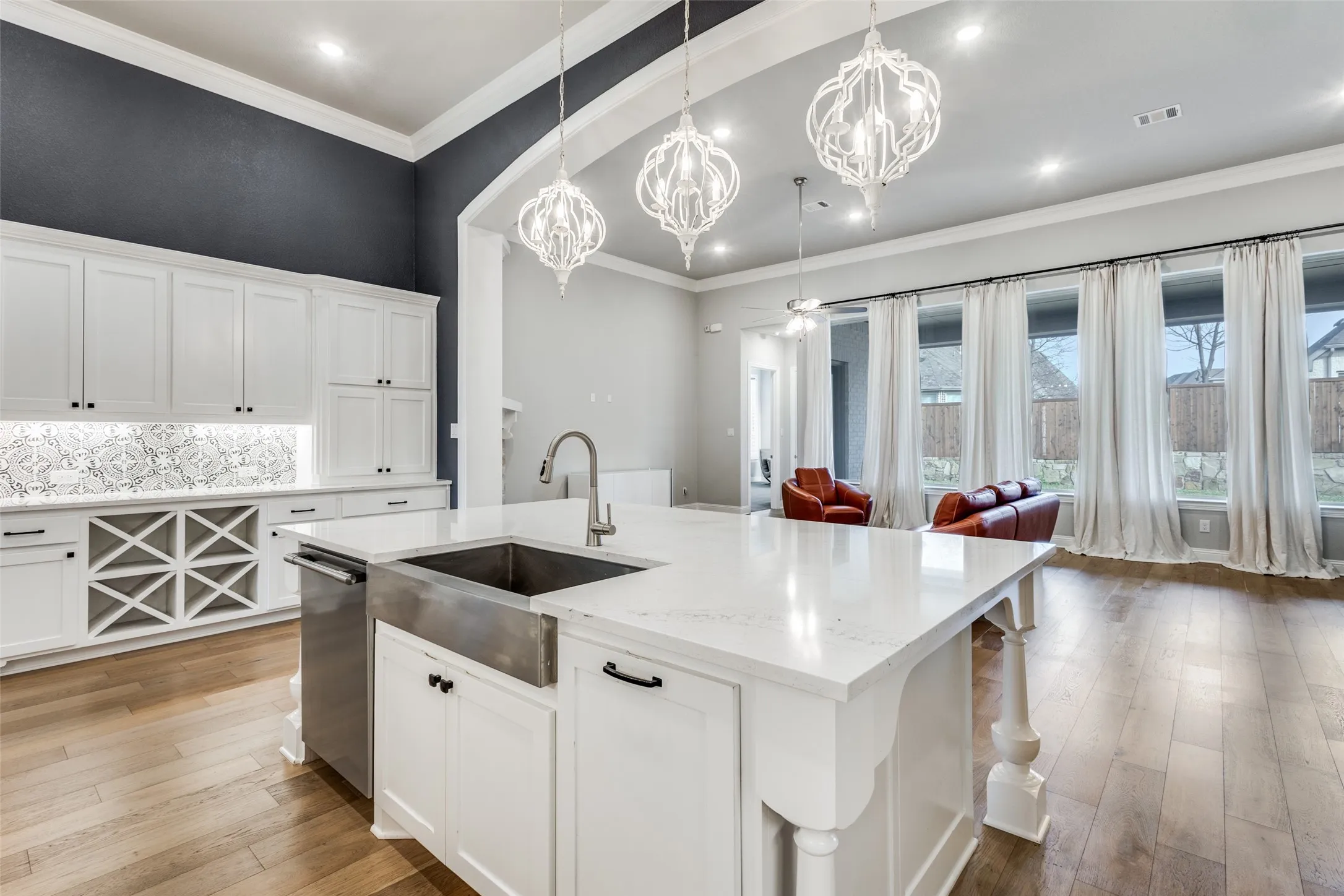 Kitchen featuring white cabinetry, light wood-style flooring, light stone countertops, a kitchen island with sink, and ornamental molding