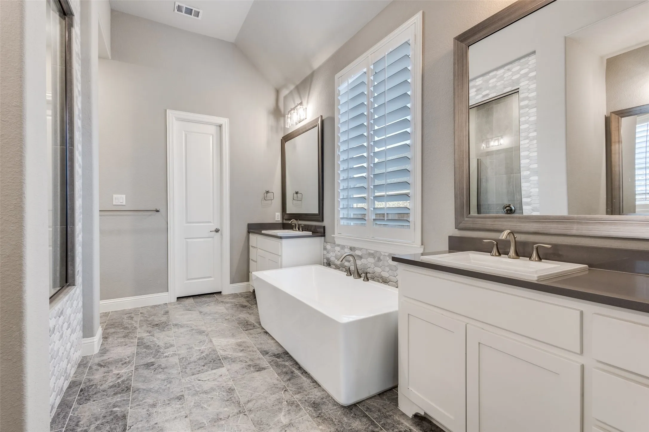 Primary Bathroom with a freestanding tub, two vanities, lofted ceiling, and healthy amount of natural light