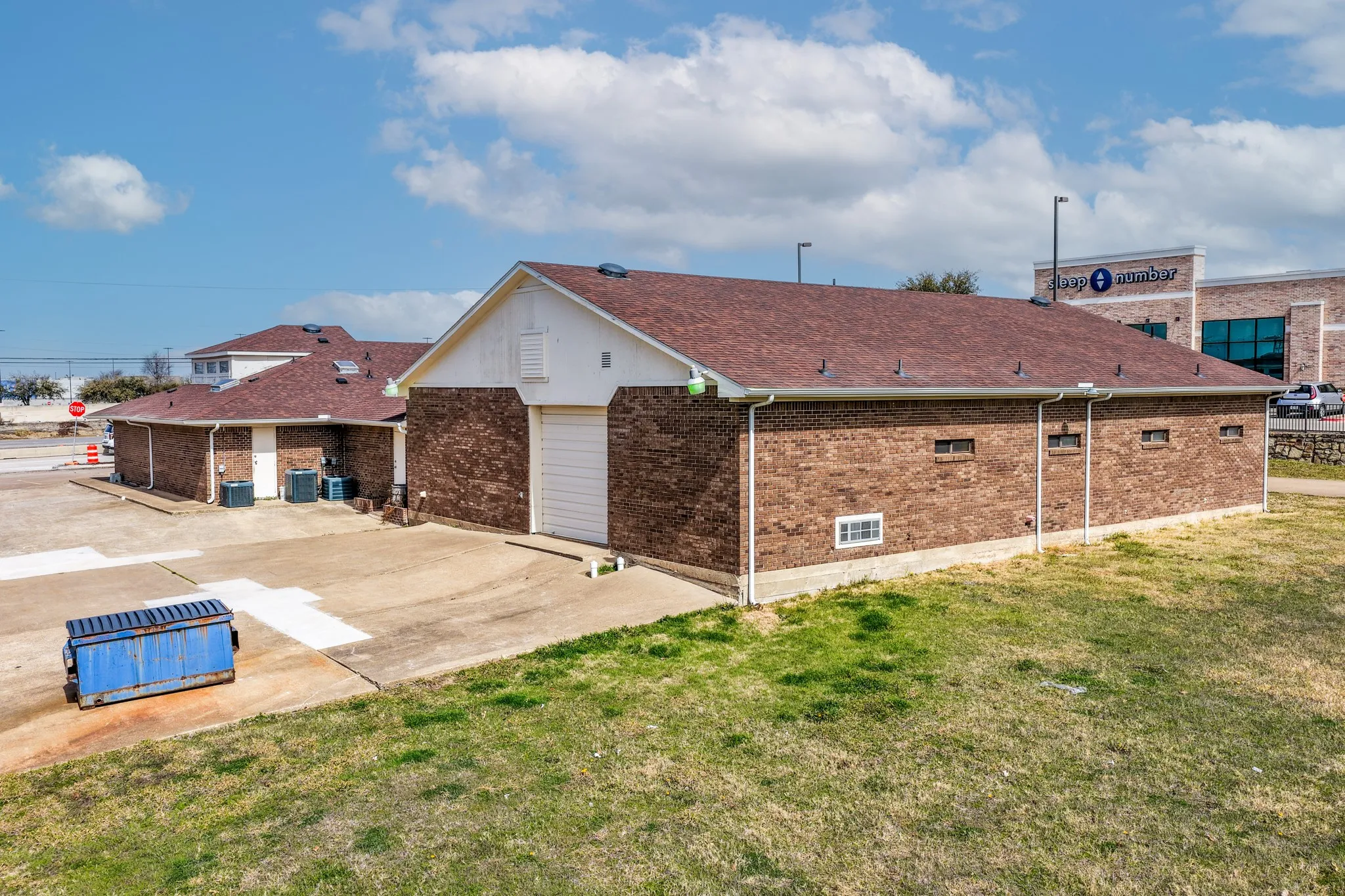 View of side of property with brick siding, a lawn, a garage, driveway, and a shingled roof