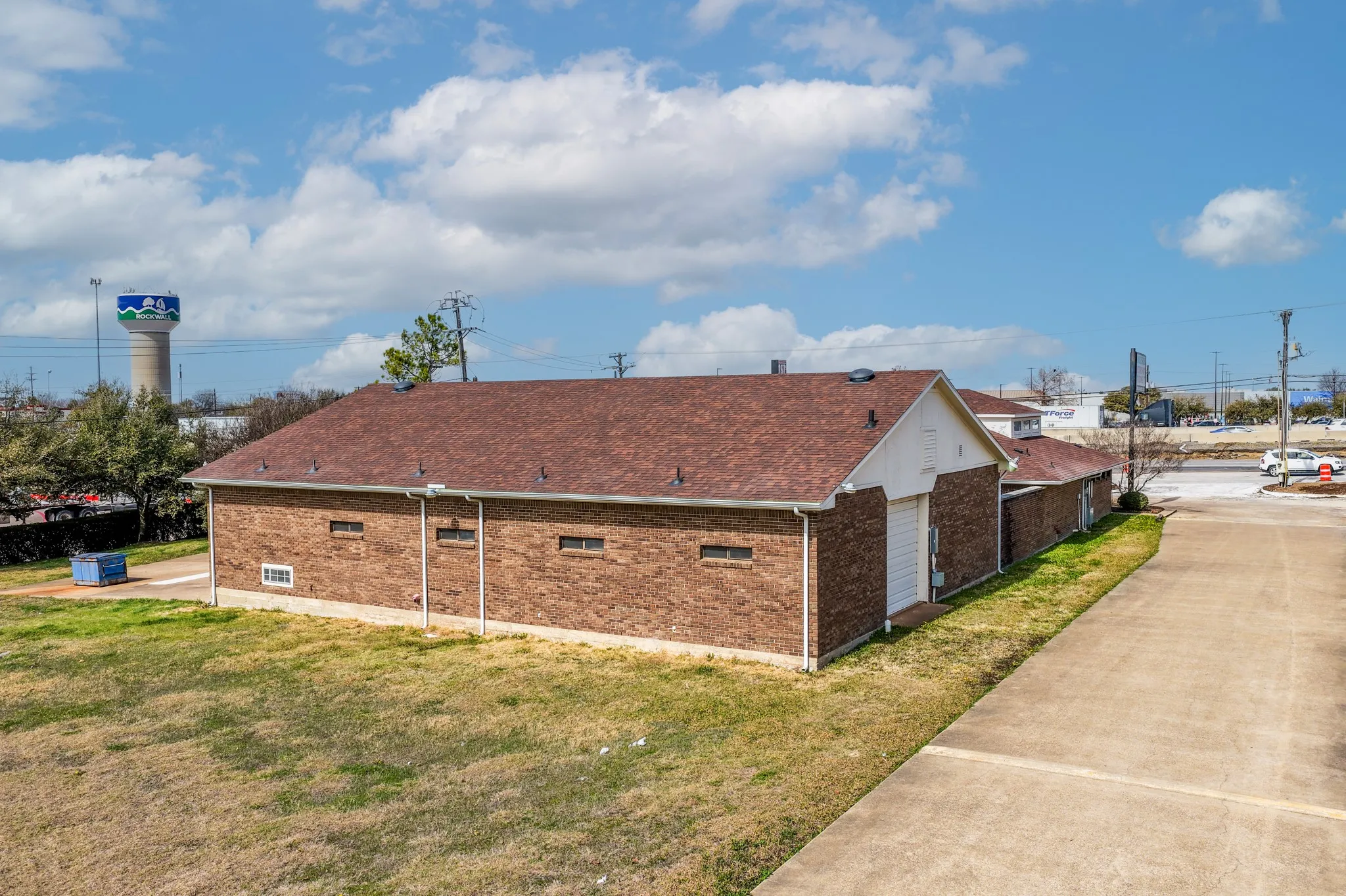 View of property exterior featuring brick siding, roof with shingles, and a lawn