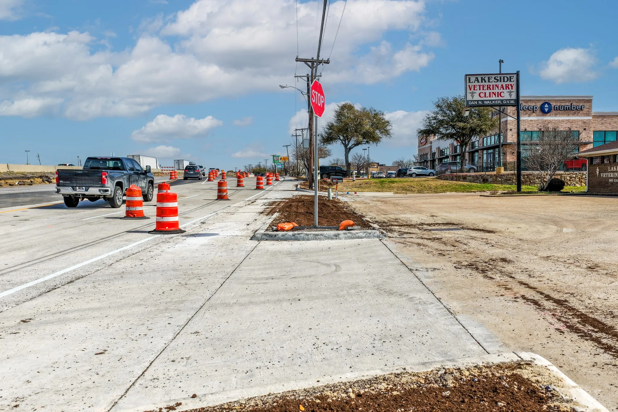 View of concrete road featuring street lighting, sidewalks, curbs, and traffic signs