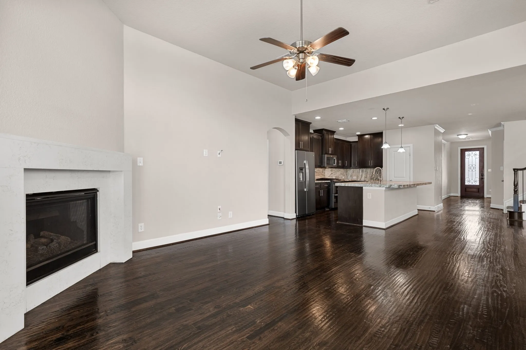 Unfurnished living room with a glass covered fireplace, ceiling fan, dark wood finished floors, and arched walkways