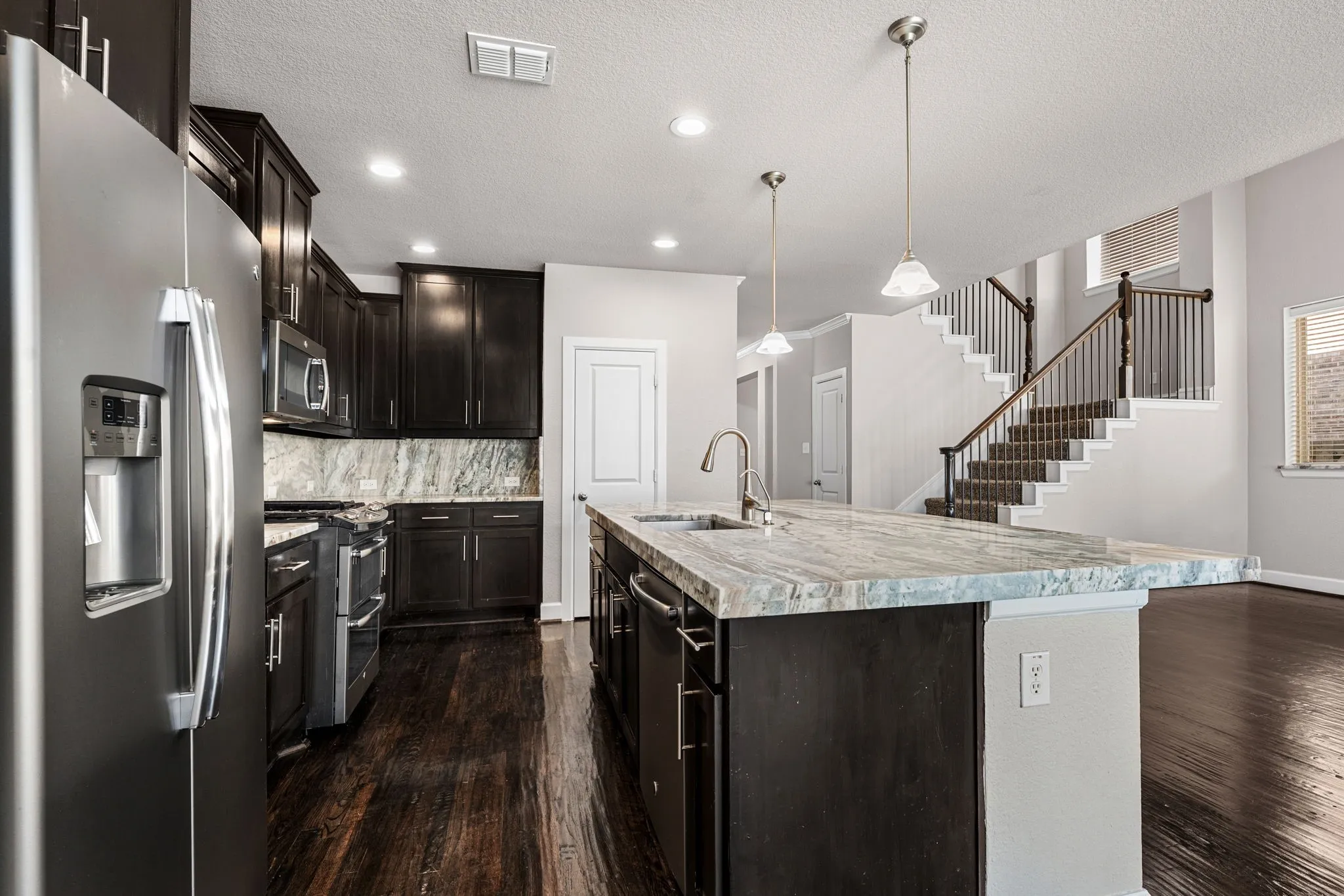 Kitchen featuring stainless steel appliances, a textured ceiling, an island with sink, decorative light fixtures, and decorative backsplash