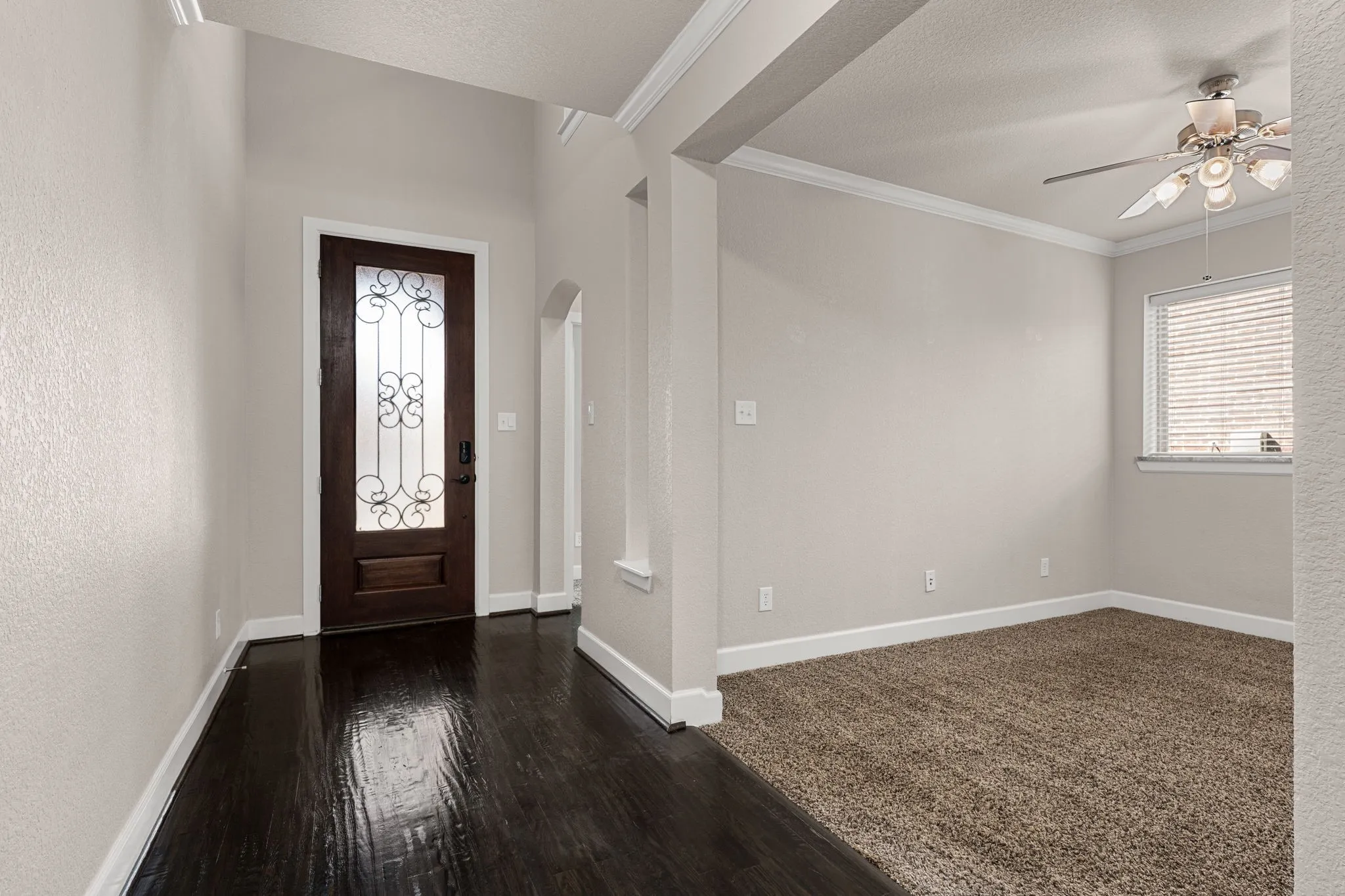 Foyer entrance with a textured ceiling, ceiling fan, arched walkways, ornamental molding, and dark wood-style floors