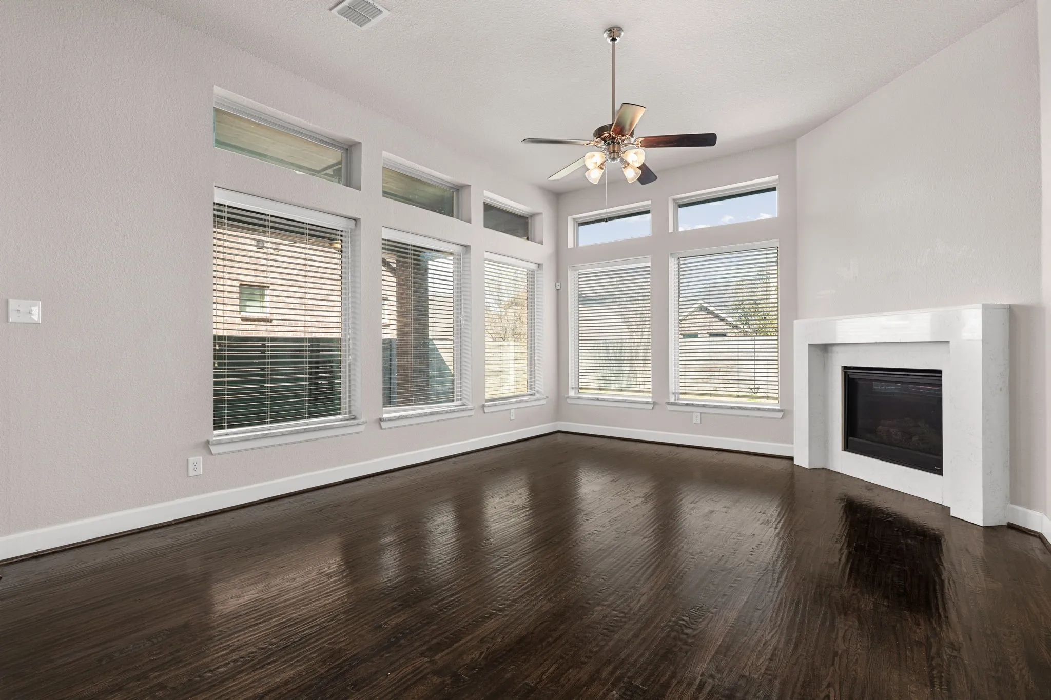 Unfurnished living room with a ceiling fan, a glass covered fireplace, and dark wood finished floors
