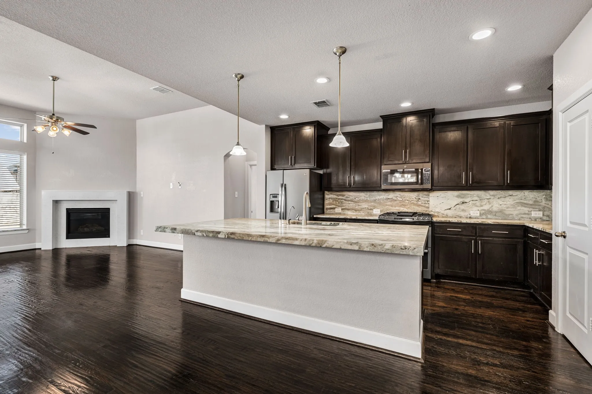 Kitchen featuring dark wood finish cabinets, a glass covered fireplace, light stone countertops, open floor plan, and stainless steel appliances
