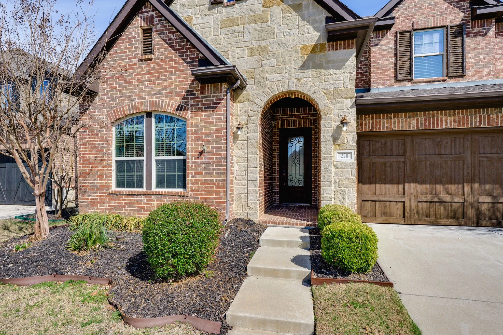 View of exterior entry featuring brick siding, driveway, stone siding, and a garage