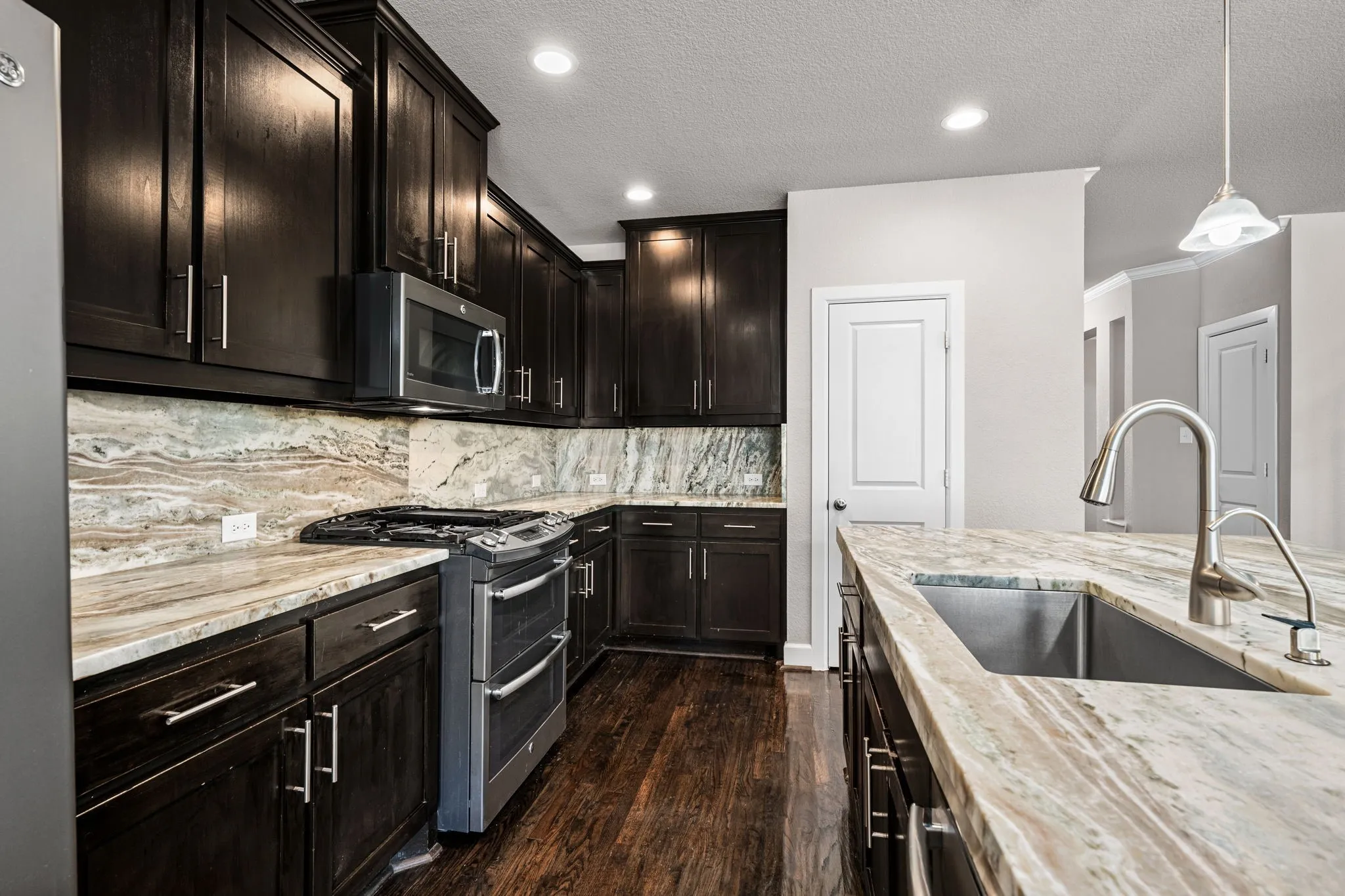 Kitchen with stainless steel appliances, light stone countertops, dark wood finish cabinetry, dark wood finished floors, and backsplash