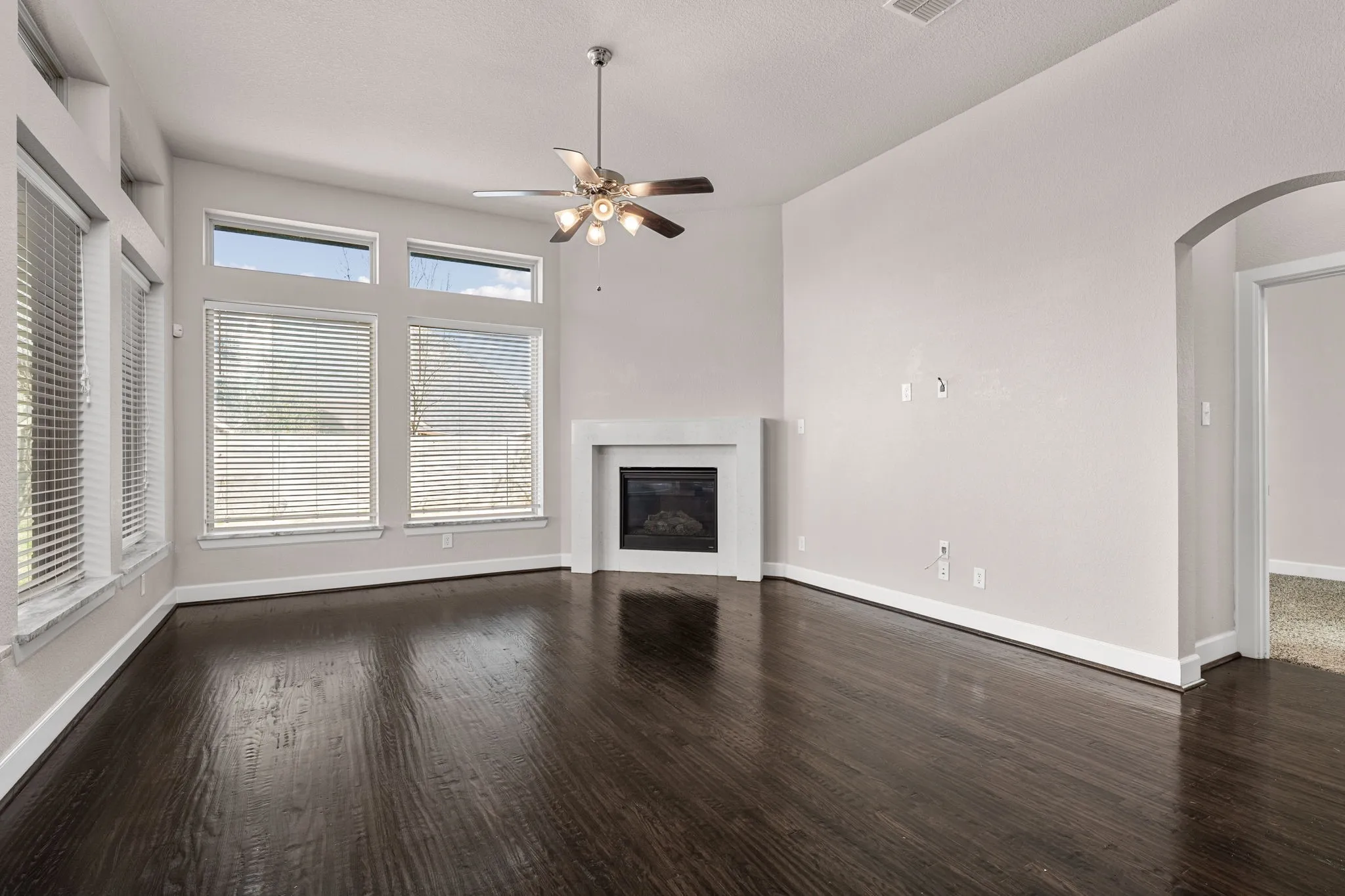 Unfurnished living room with ceiling fan, arched walkways, a glass covered fireplace, and dark wood-style floors