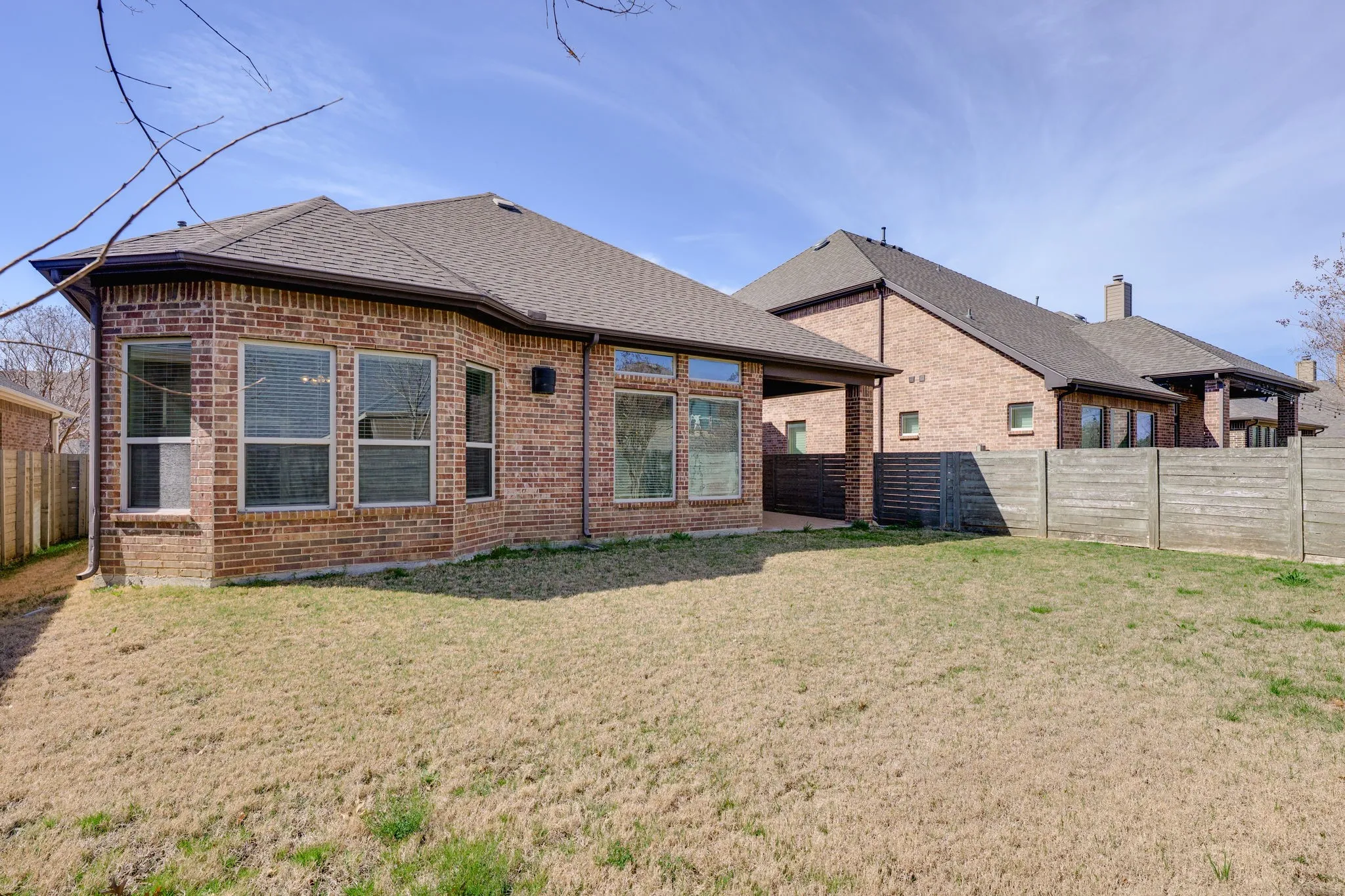 Rear view of house with brick siding, a fenced backyard, roof with shingles, and a patio area