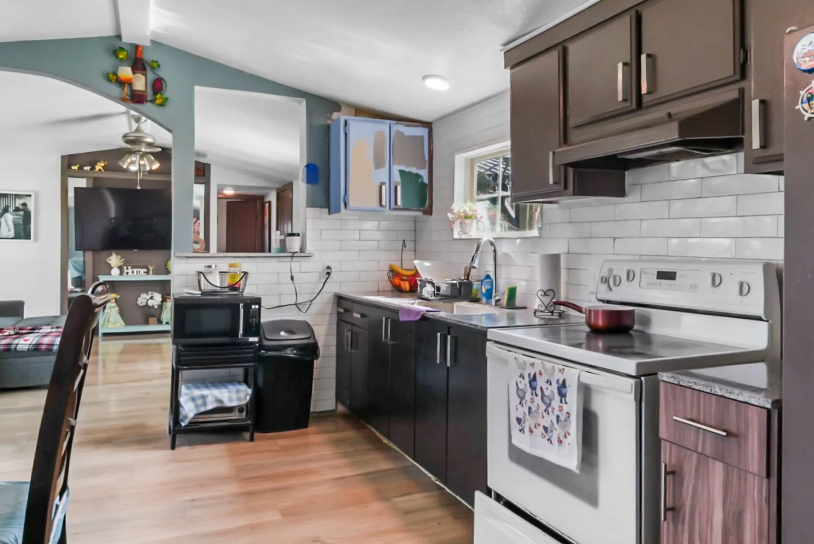 Kitchen with white range with electric stovetop, light wood finished floors, lofted ceiling, black microwave, and decorative backsplash