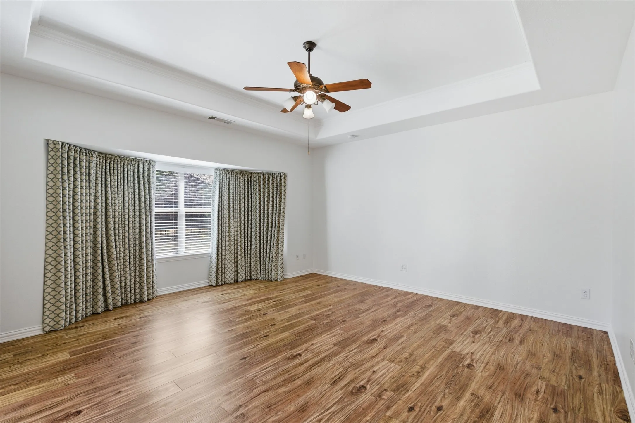 Spacious primary bedroom with a tray ceiling and bay window