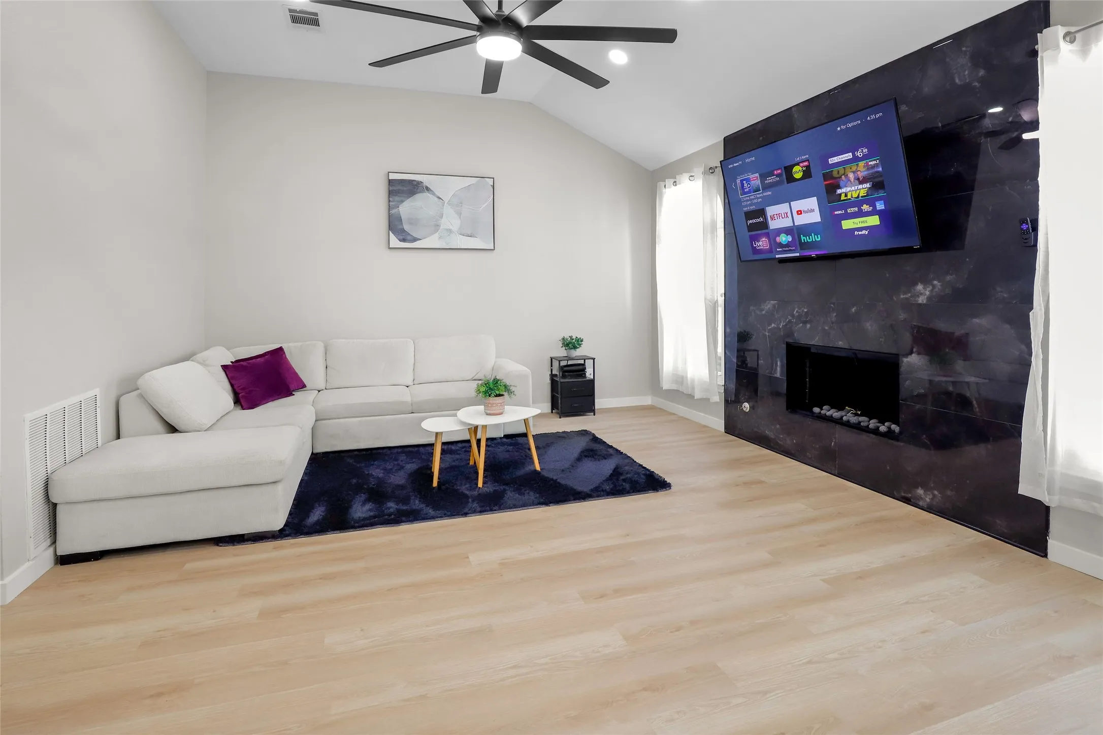 Living room with ceiling fan, wood finished floors, vaulted ceiling, and a high end fireplace