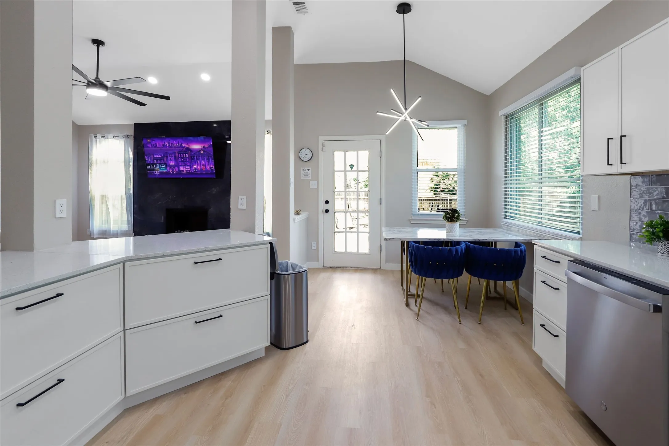 Kitchen with stainless steel dishwasher, vaulted ceiling, light wood-type flooring, white cabinets, and ceiling fan