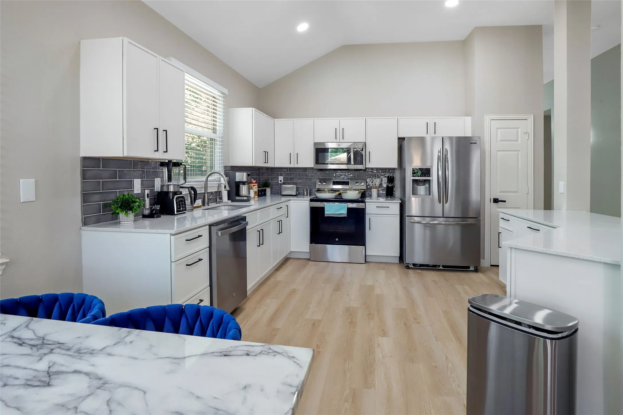 Kitchen featuring appliances with stainless steel finishes, light wood-style floors, decorative backsplash, white cabinets, and light countertops