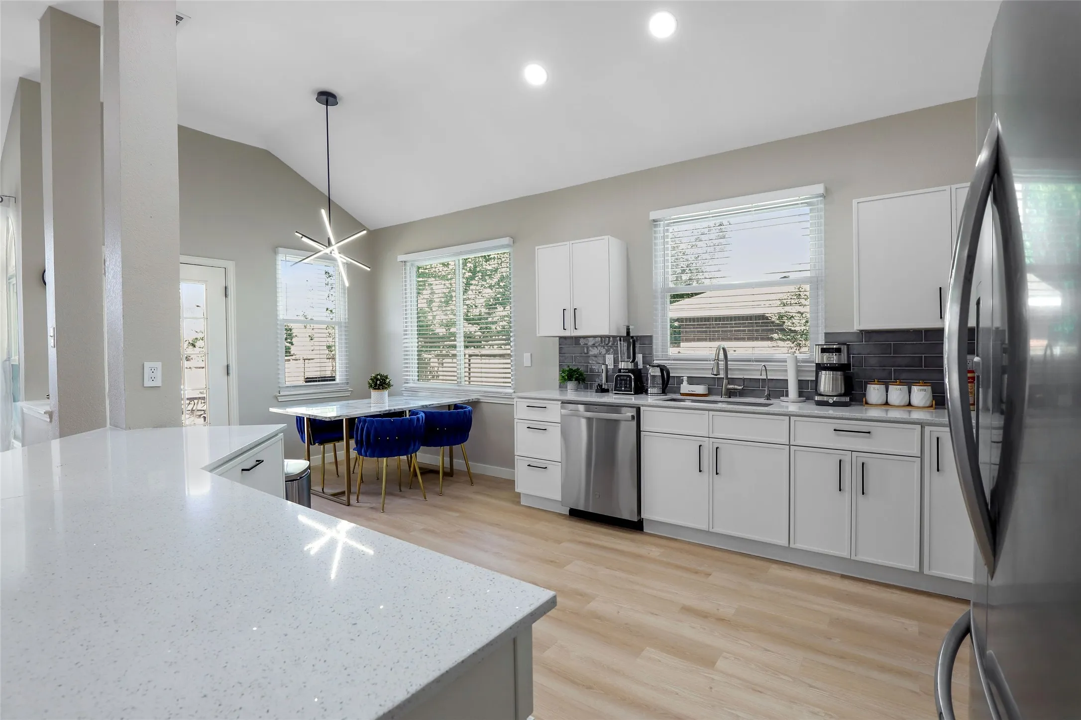Kitchen featuring appliances with stainless steel finishes, tasteful backsplash, light wood finished floors, white cabinets, and decorative light fixtures