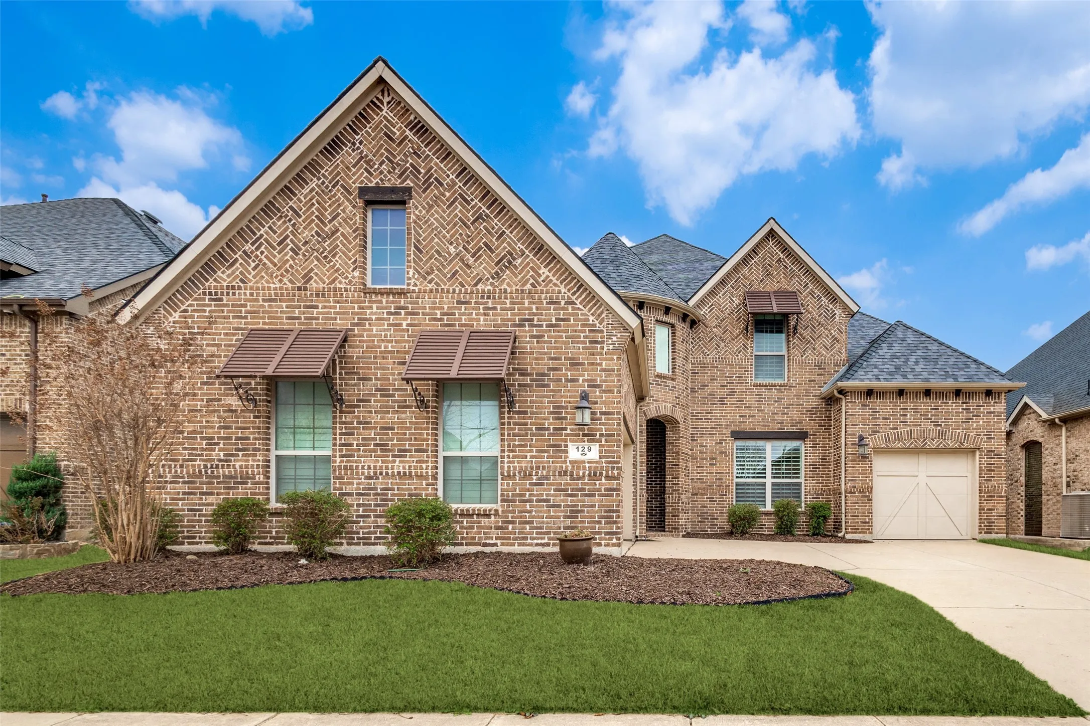 View of front of house with brick siding, a front lawn, a shingled roof, an attached garage, and driveway