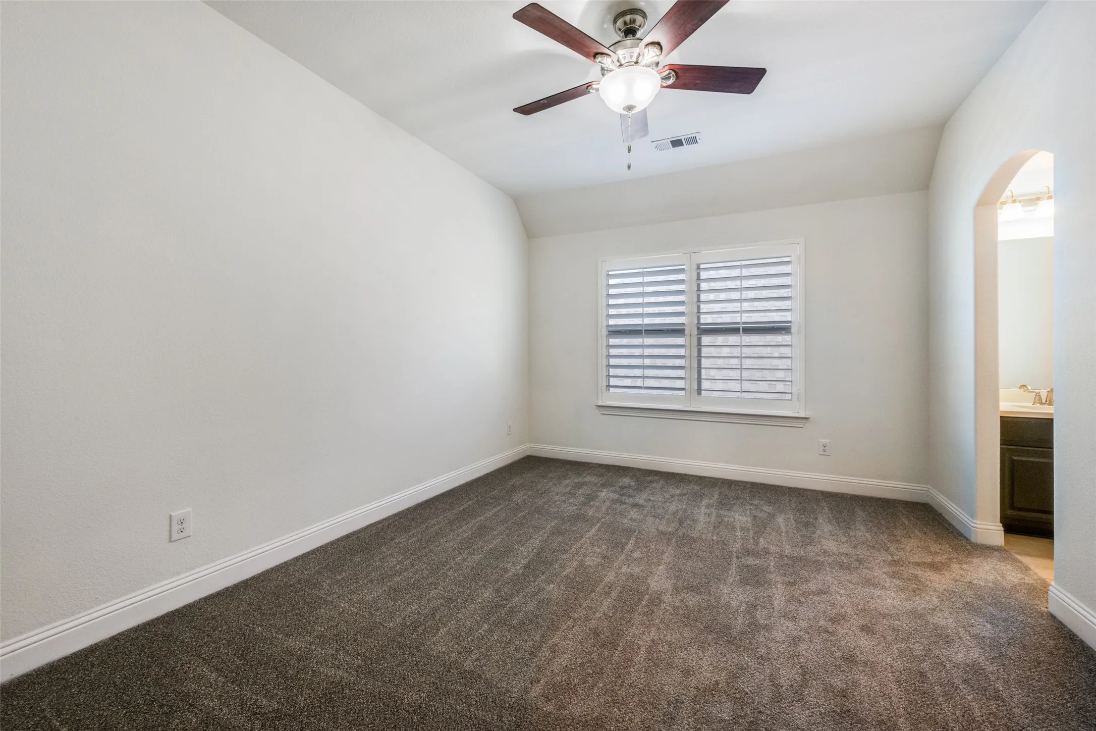 Empty room with dark colored carpet, ceiling fan, arched walkways, and vaulted ceiling