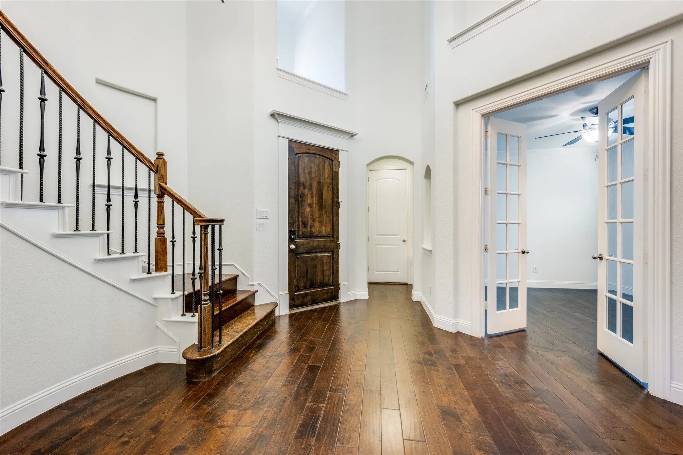 Entrance foyer featuring a high ceiling, ceiling fan, dark wood-style floors, arched walkways, and french doors