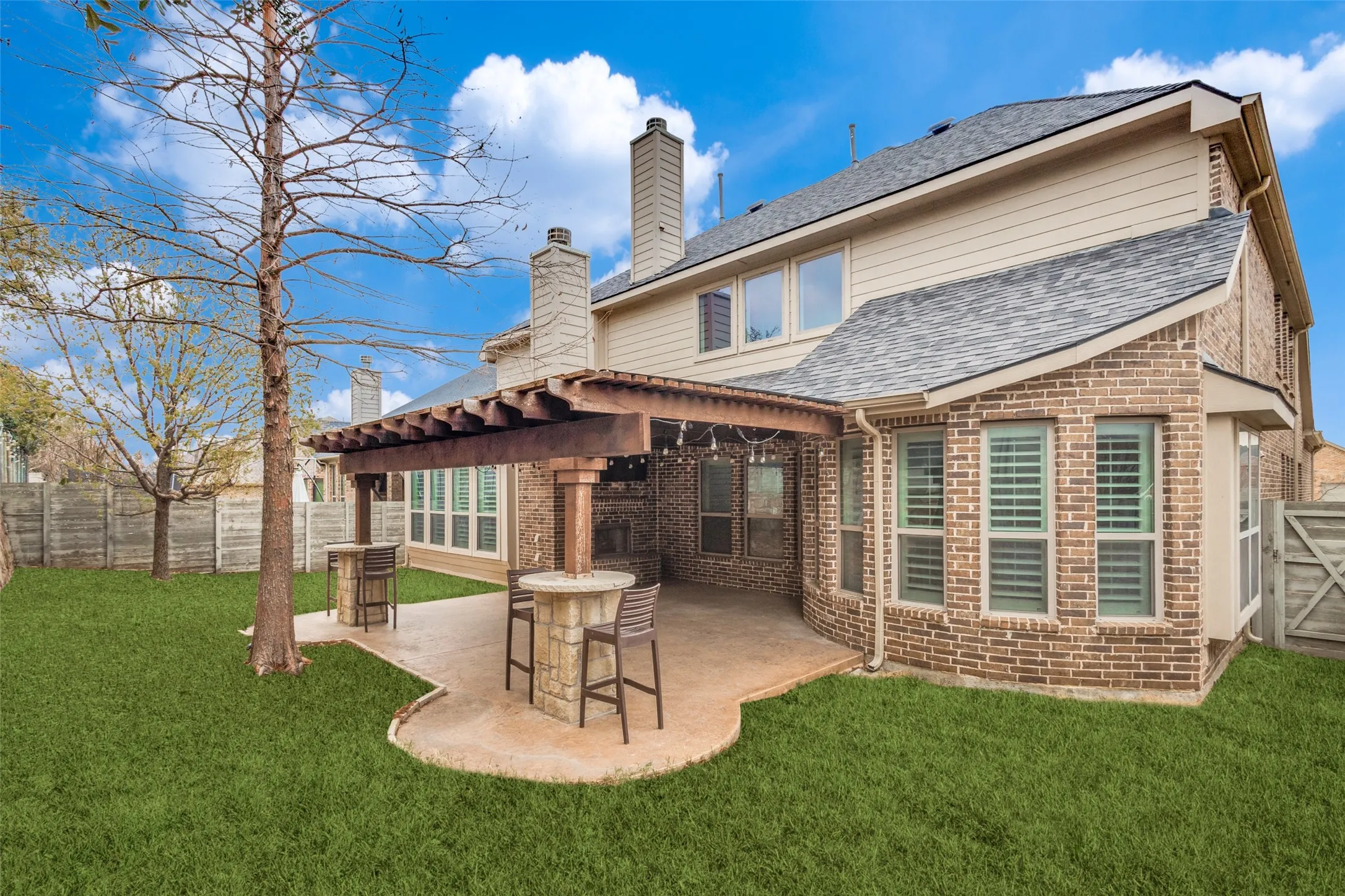 Back of property featuring brick siding, a fenced backyard, a patio area, and a shingled roof