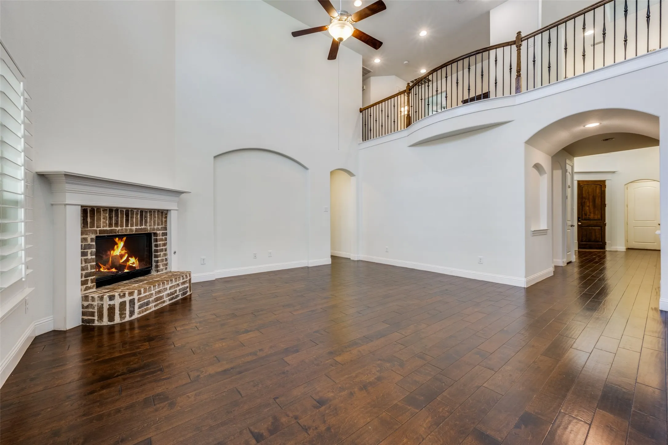 Unfurnished living room with a ceiling fan, arched walkways, a fireplace, dark wood-style flooring, and a high ceiling