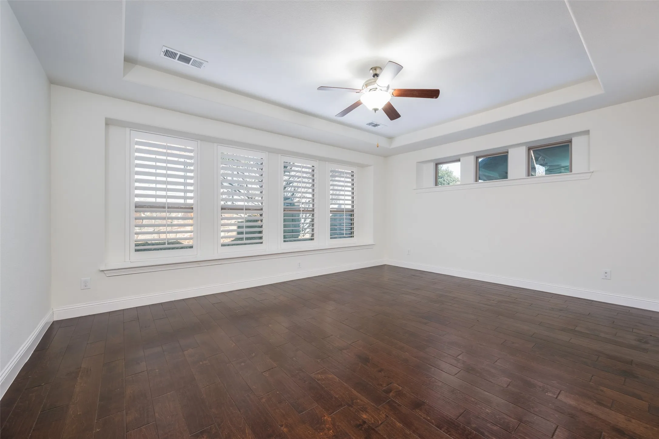 Empty room featuring a tray ceiling, ceiling fan, and dark wood-type flooring