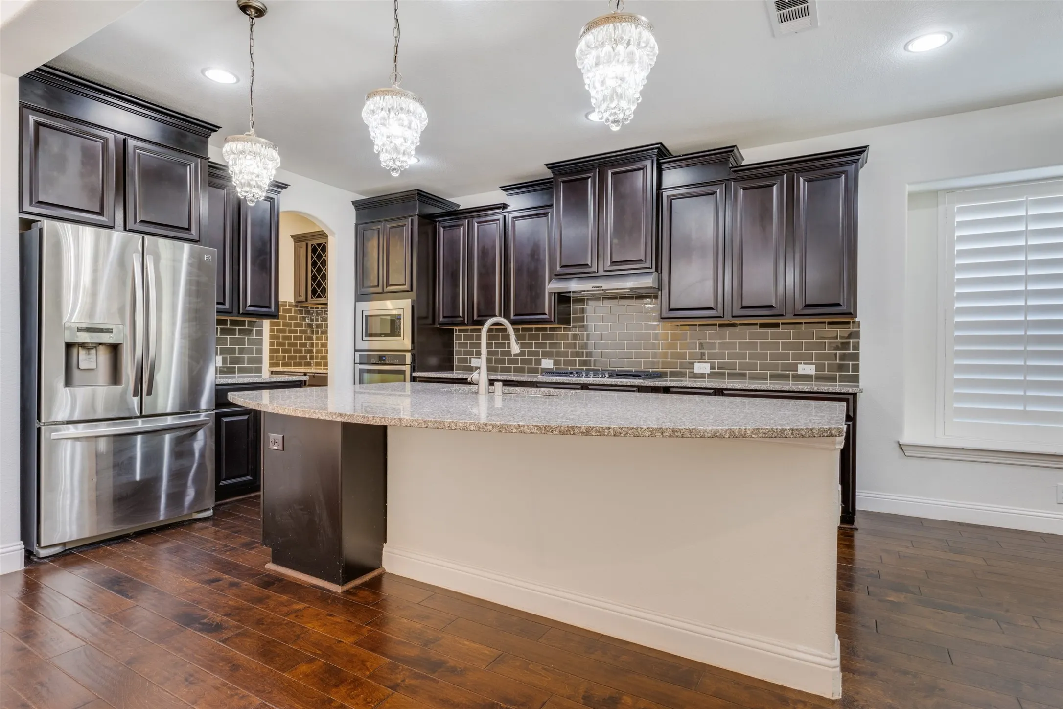Kitchen with stainless steel appliances, arched walkways, dark wood finish cabinets, and a center island with sink