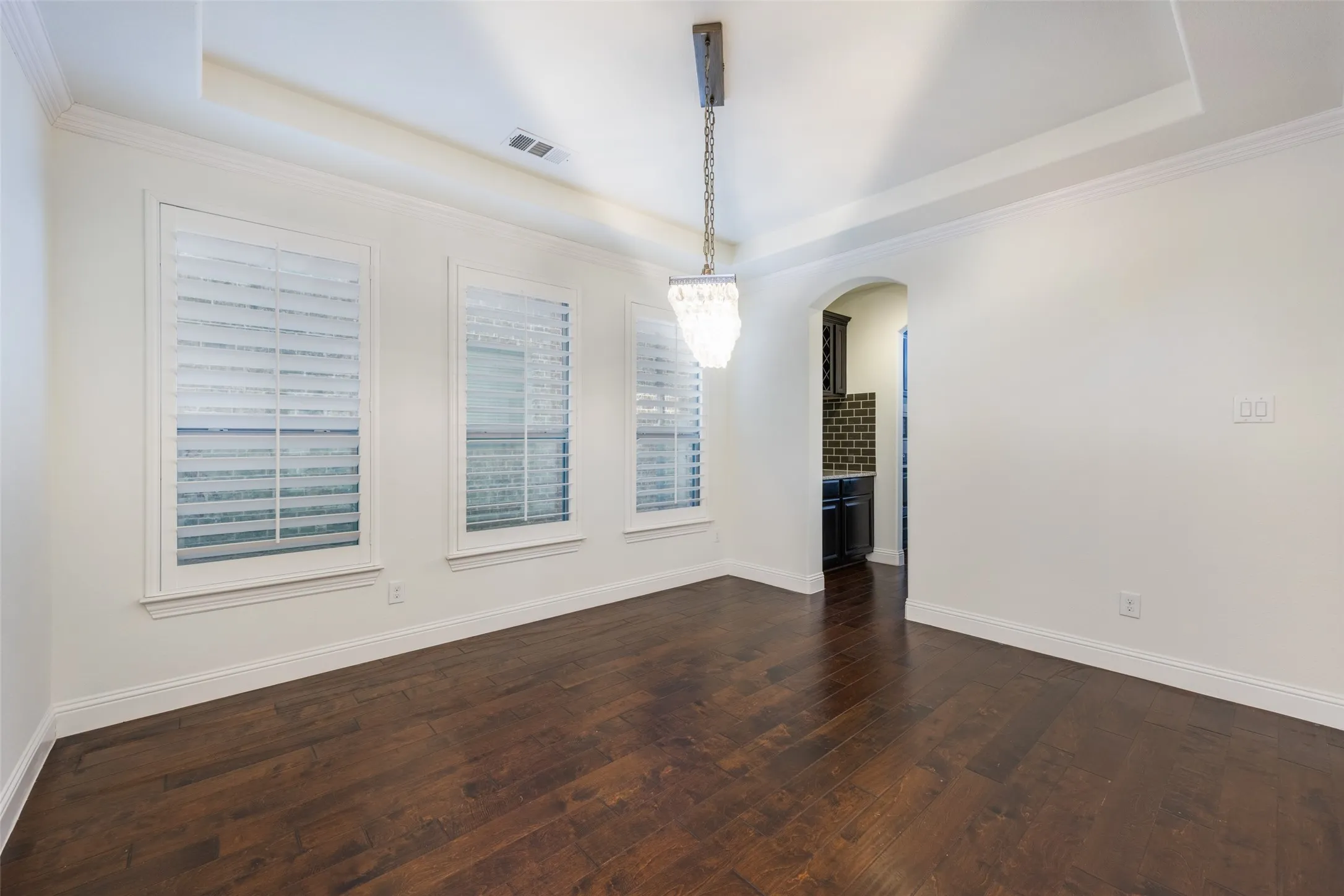 Unfurnished dining area featuring a tray ceiling, arched walkways, dark wood-type flooring, and crown molding