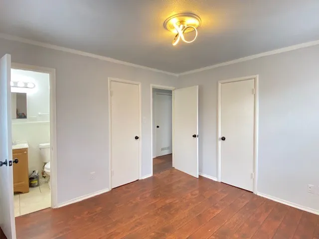 Unfurnished bedroom featuring two closets, dark wood finished floors, crown molding, and connected bathroom