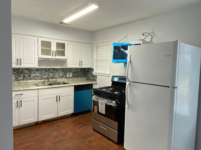 Kitchen with white cabinets, freestanding refrigerator, stainless steel gas range oven, and dark wood-style flooring